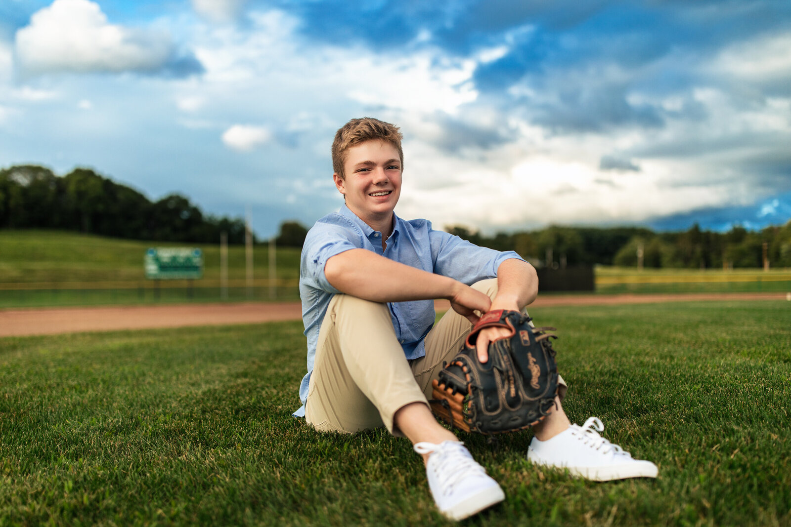 A senior student hold his ball and glove while he sits at the fields near Pennsylvania.