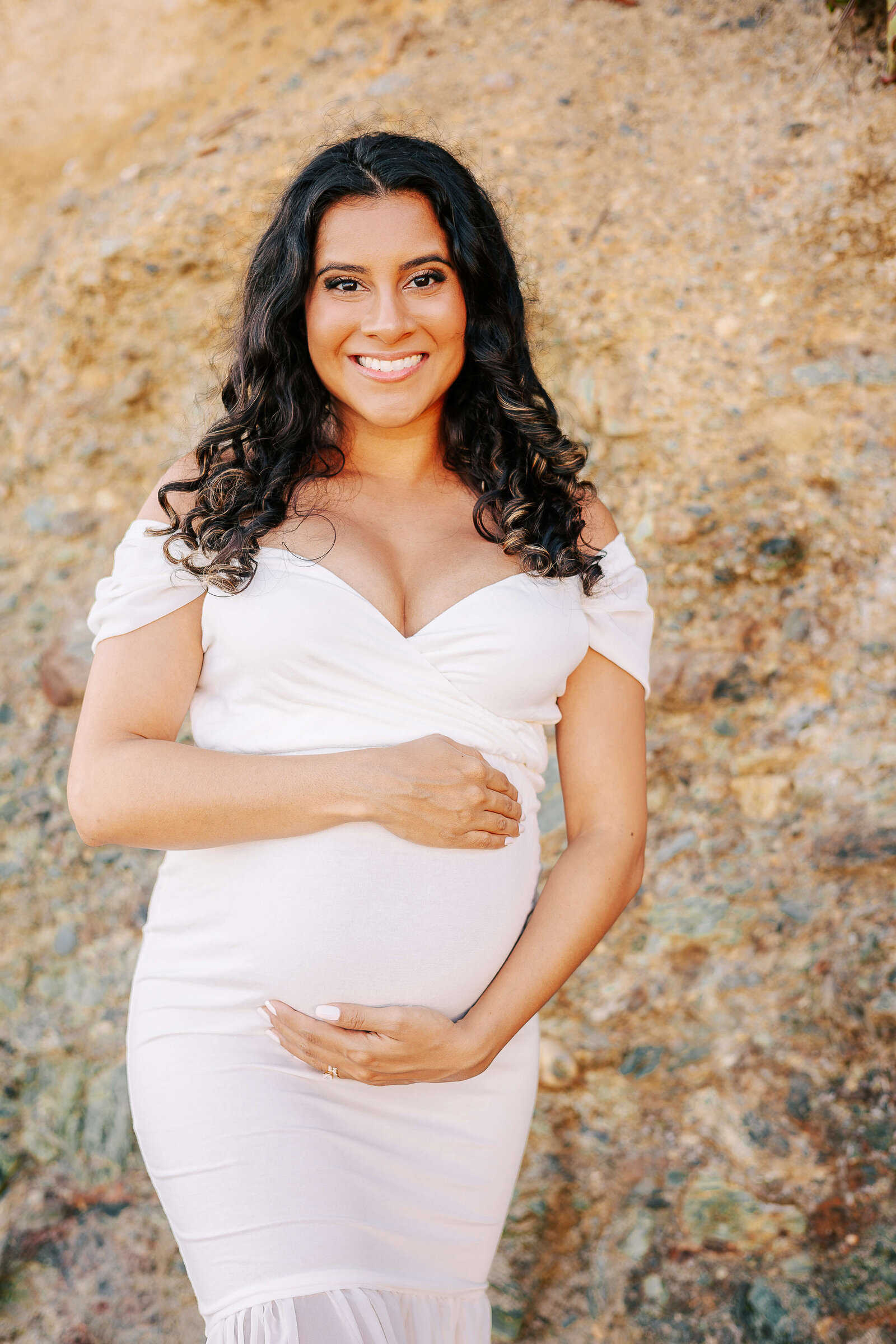 Mom holding bump at maternity session posed at rocky beach in newport beach.