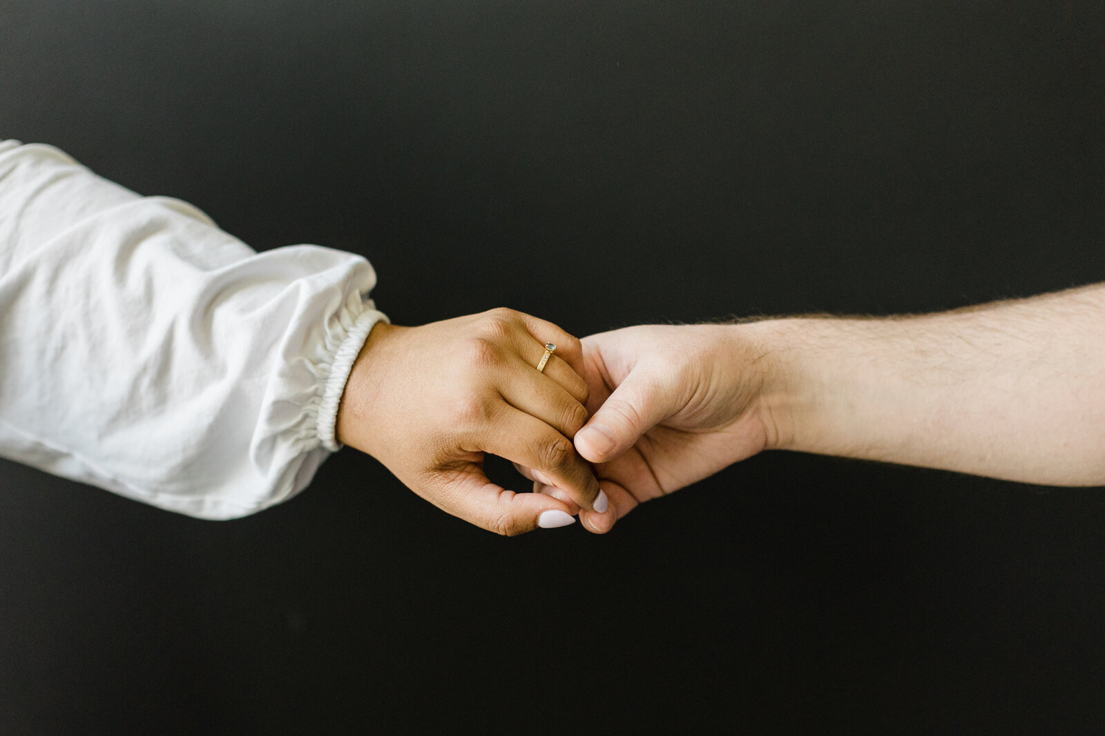 Close up photo of a couple holding hands in front of a black background.