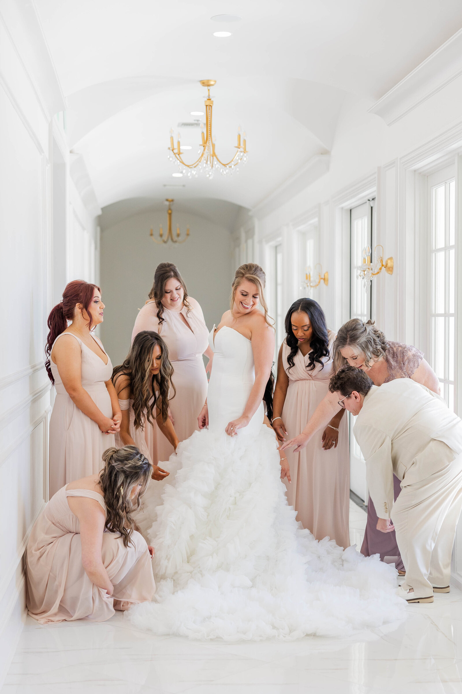 bride-with-her-bridesmaids-fluffing-her-dress-in-white-hallway