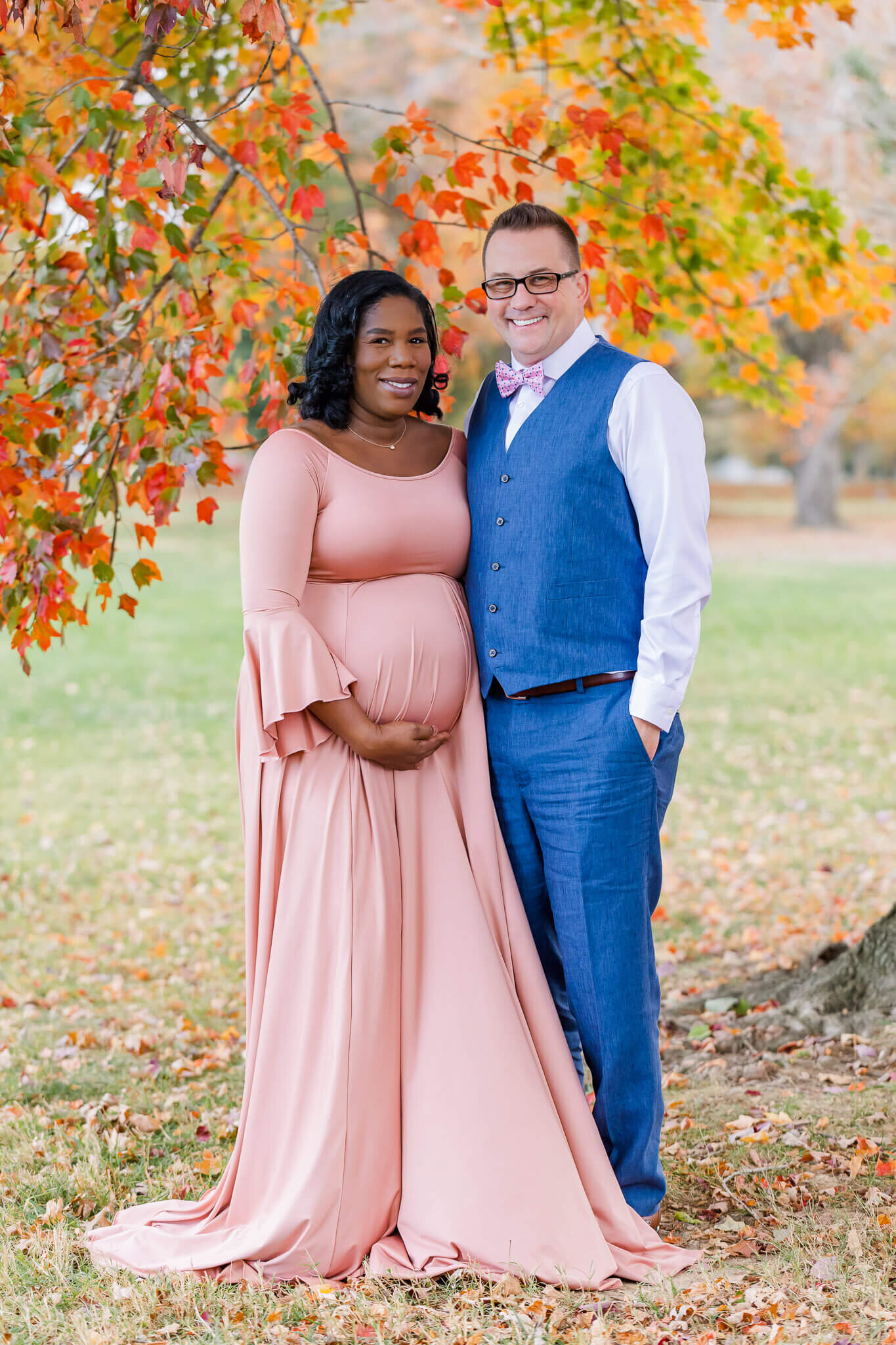 A couple posing in front of the Alexandria fall foliage during their maternity portrait session.
