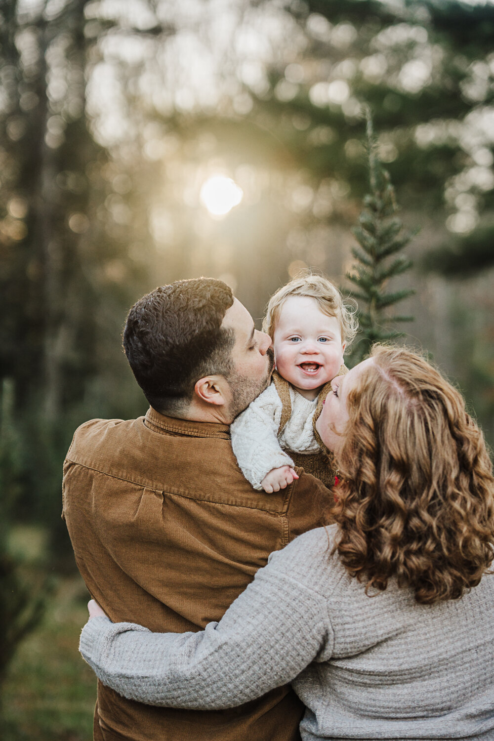 baby boy smiles over parents shoulders at tree farm