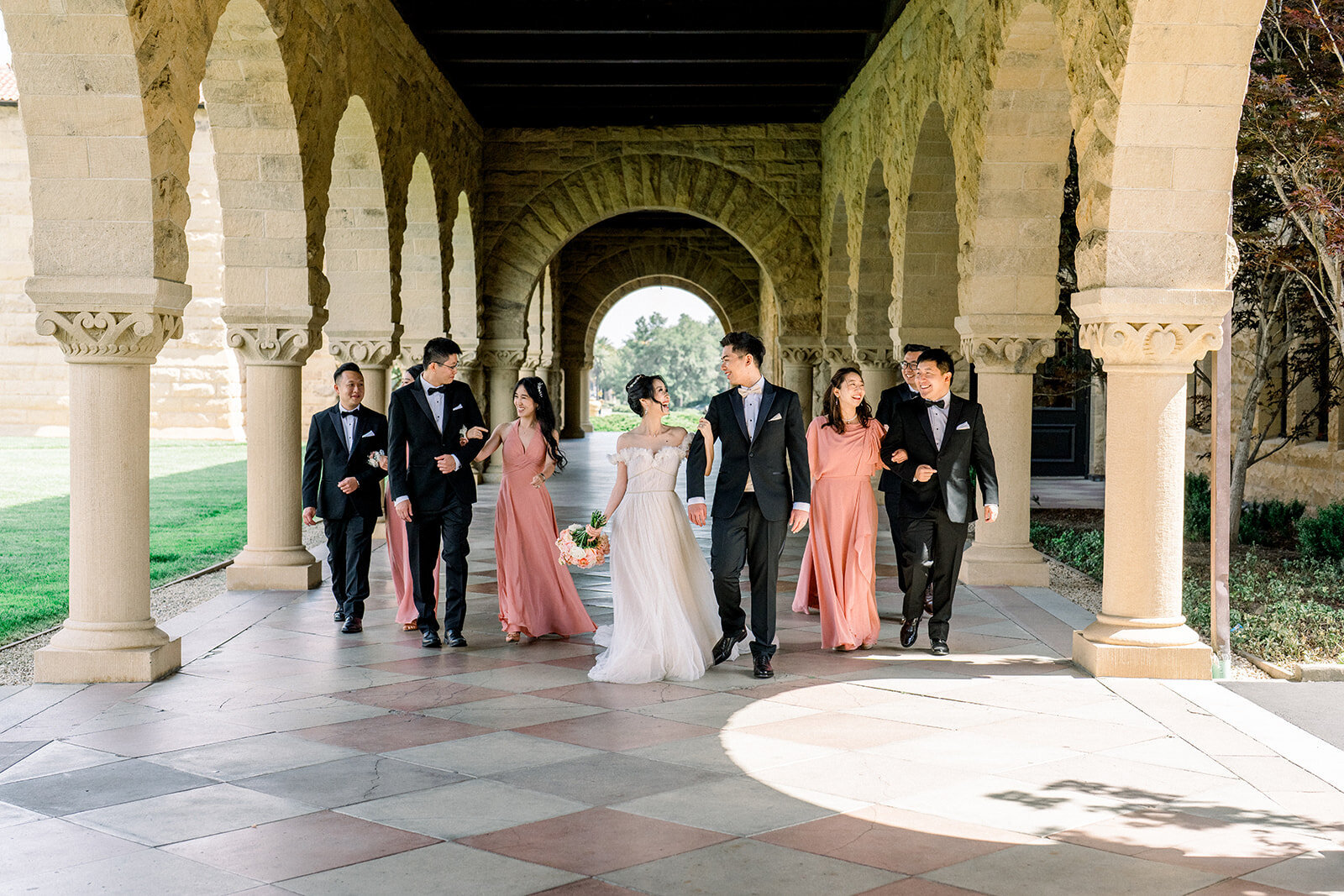 The bridal party poses under the historic arches of Stanford University, showcasing their style and joy during the wedding.