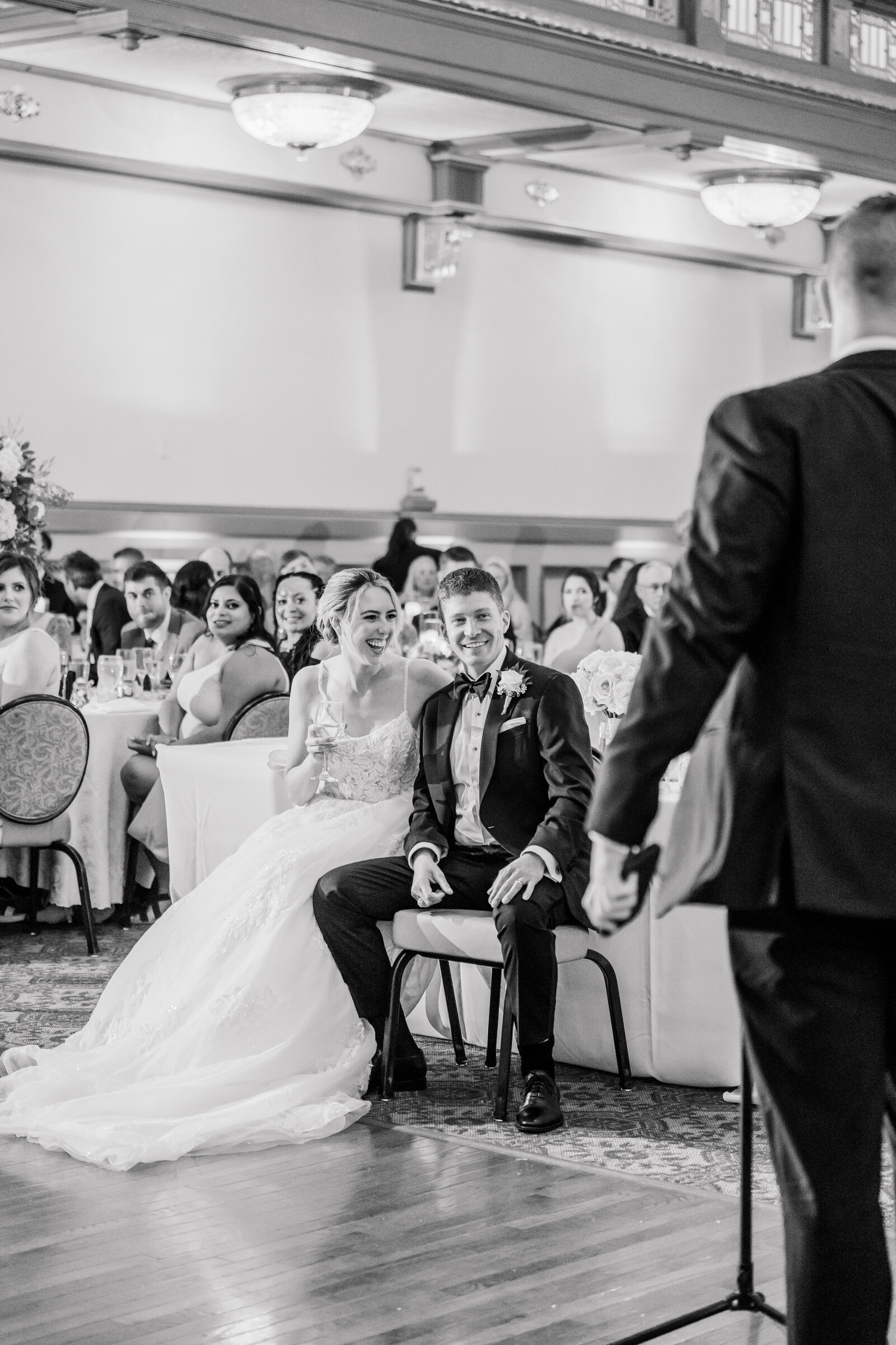 Film photograph shot on 35mm film in black and white of the bride and groom laughing together during the best man's toast