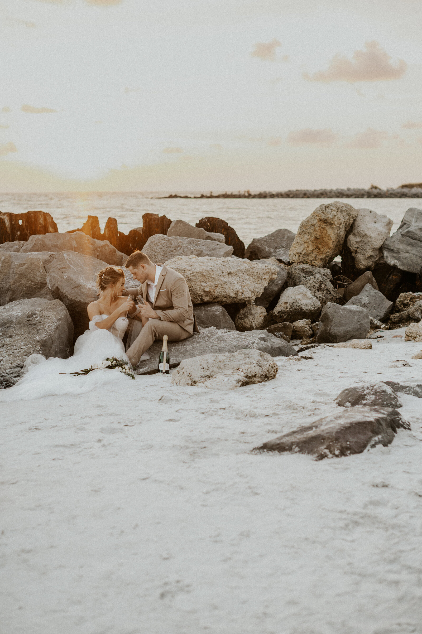 Couple sitting on the rocks while toasting champagne glasses during their Florida Elopement.