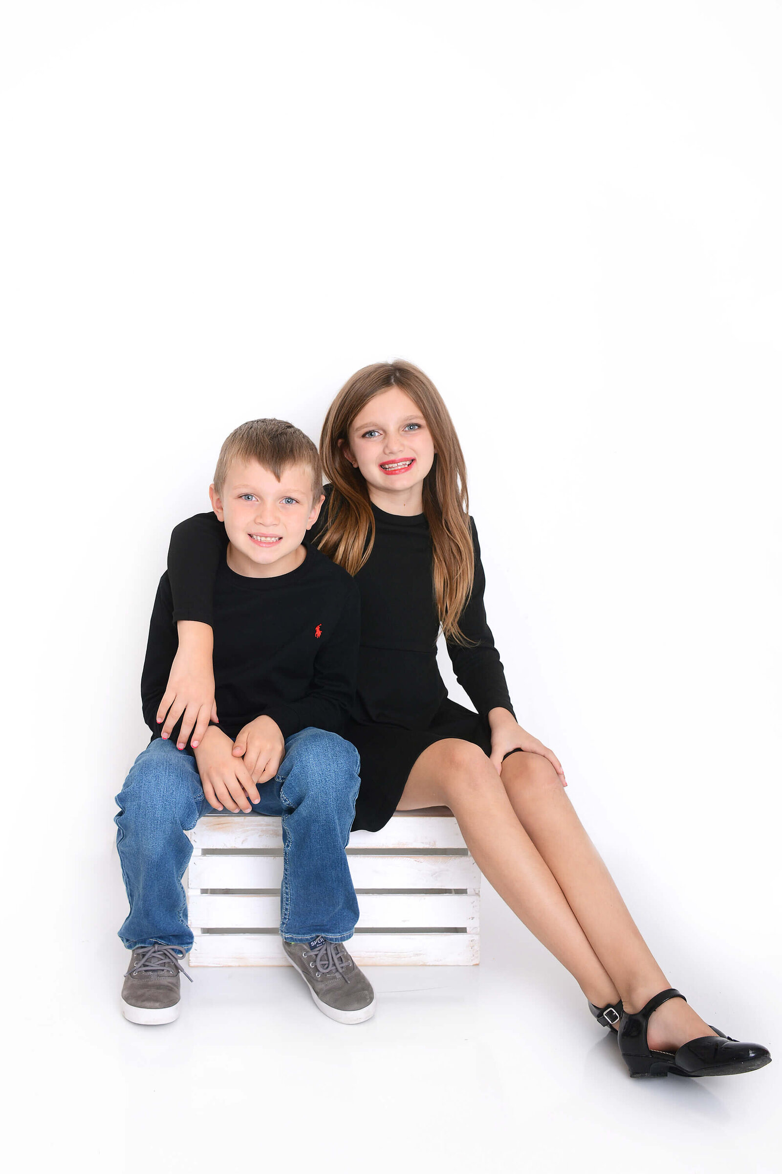 brother and sister sit on a box and smile at the camera