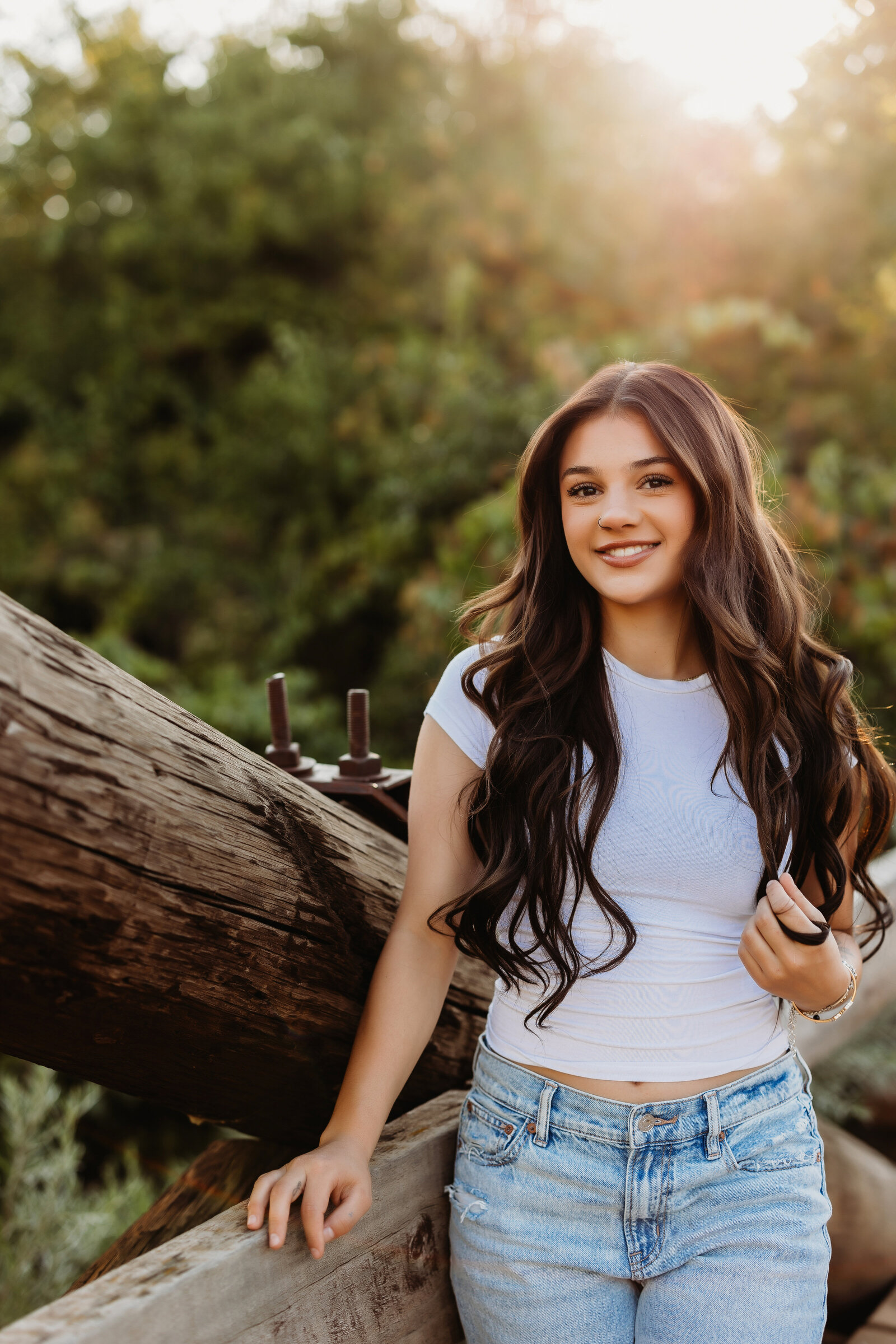 high school senior with long brown hair and white tshirt standing on wooden bridge
