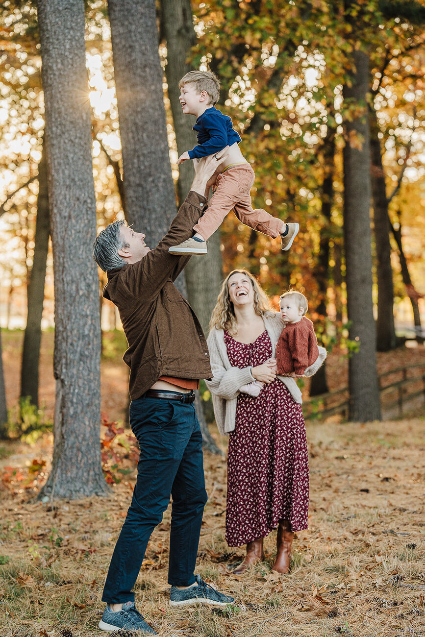 family in autumn in the woods throws son in air and laughs