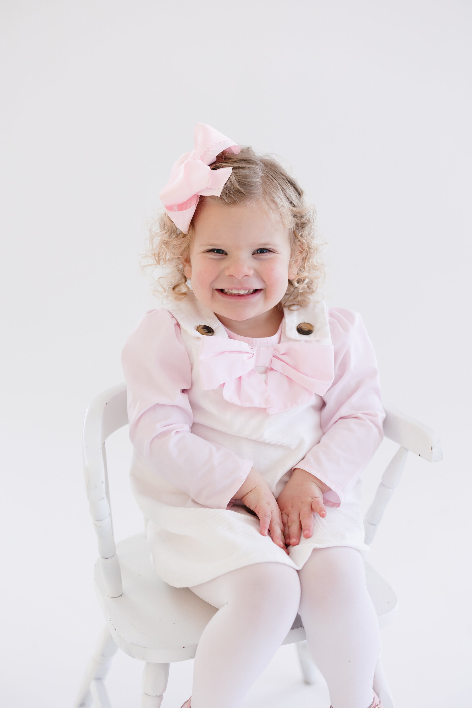 Little girl sitting on a white chair smiling at the camera
