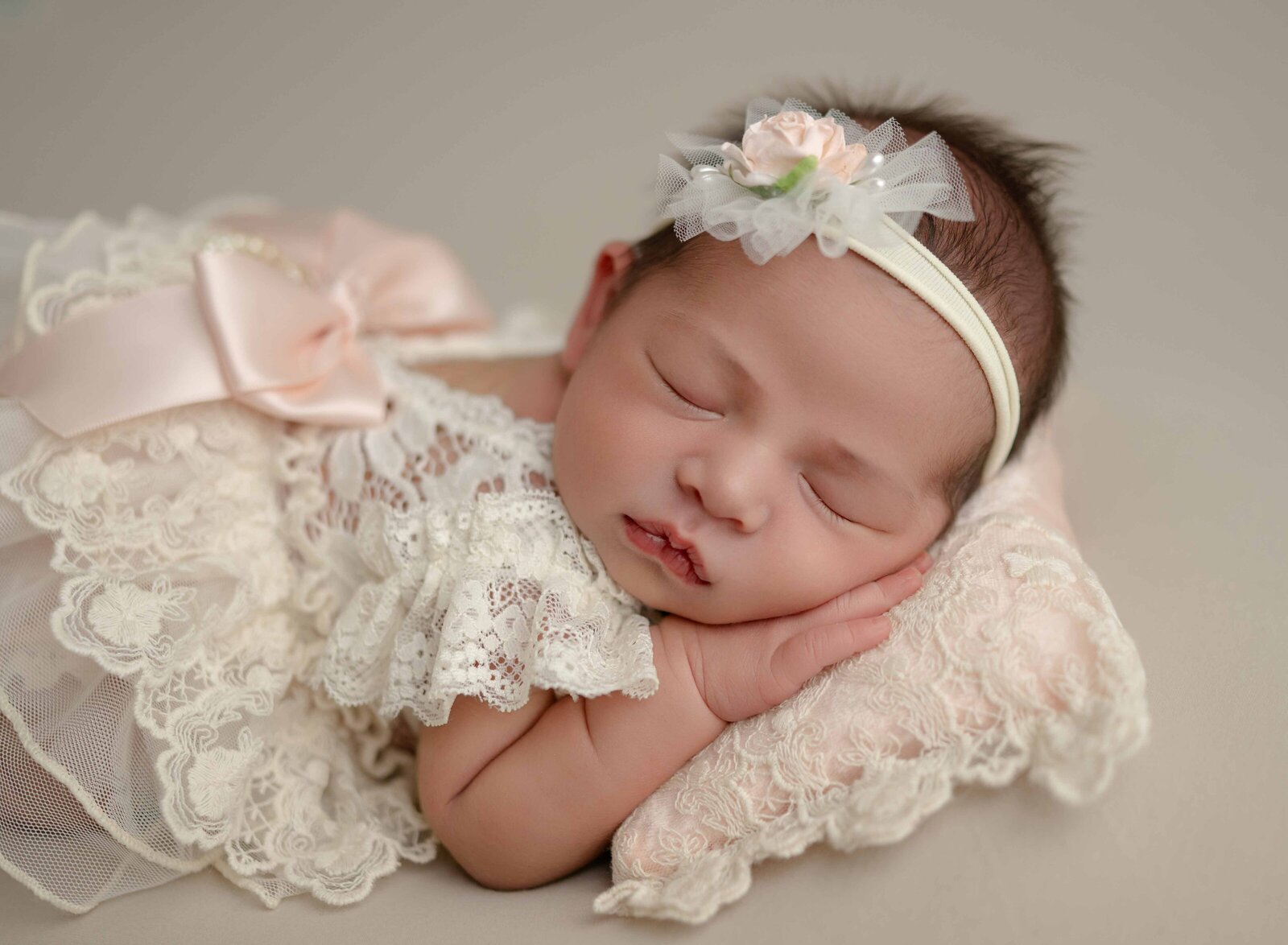 Baby girl sleeping on a lace pillow with a lace outfit and peach bow.