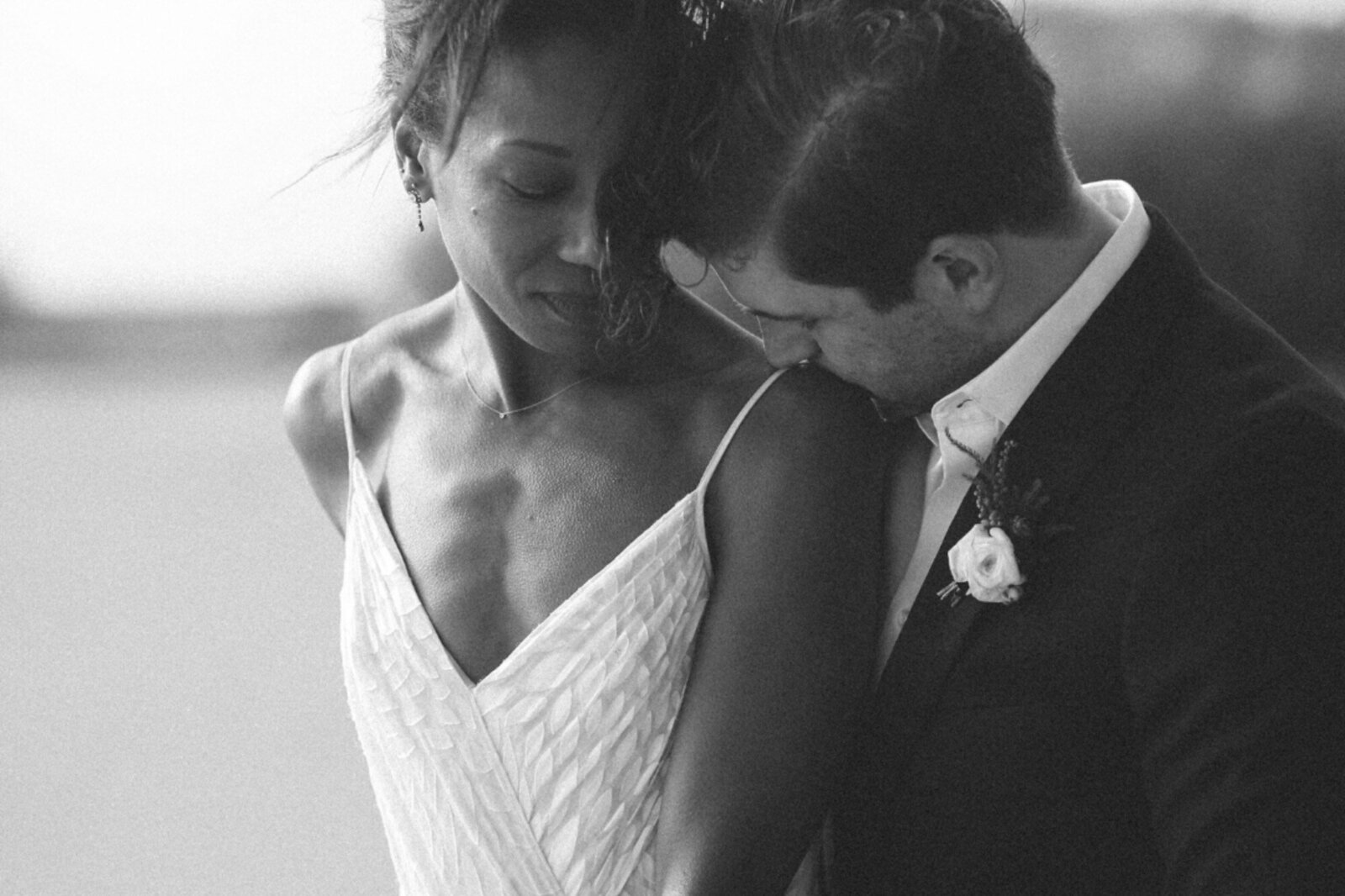 Black and white photo of the groom kissing her bride's shoulder