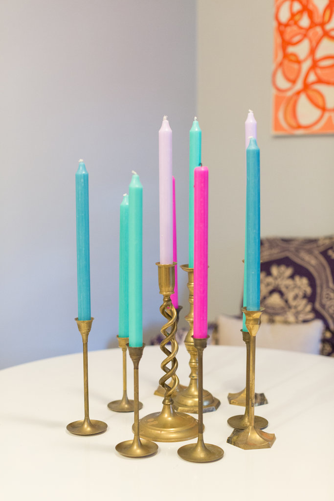 Brass candlesticks with tall, colorful candles on a white table.