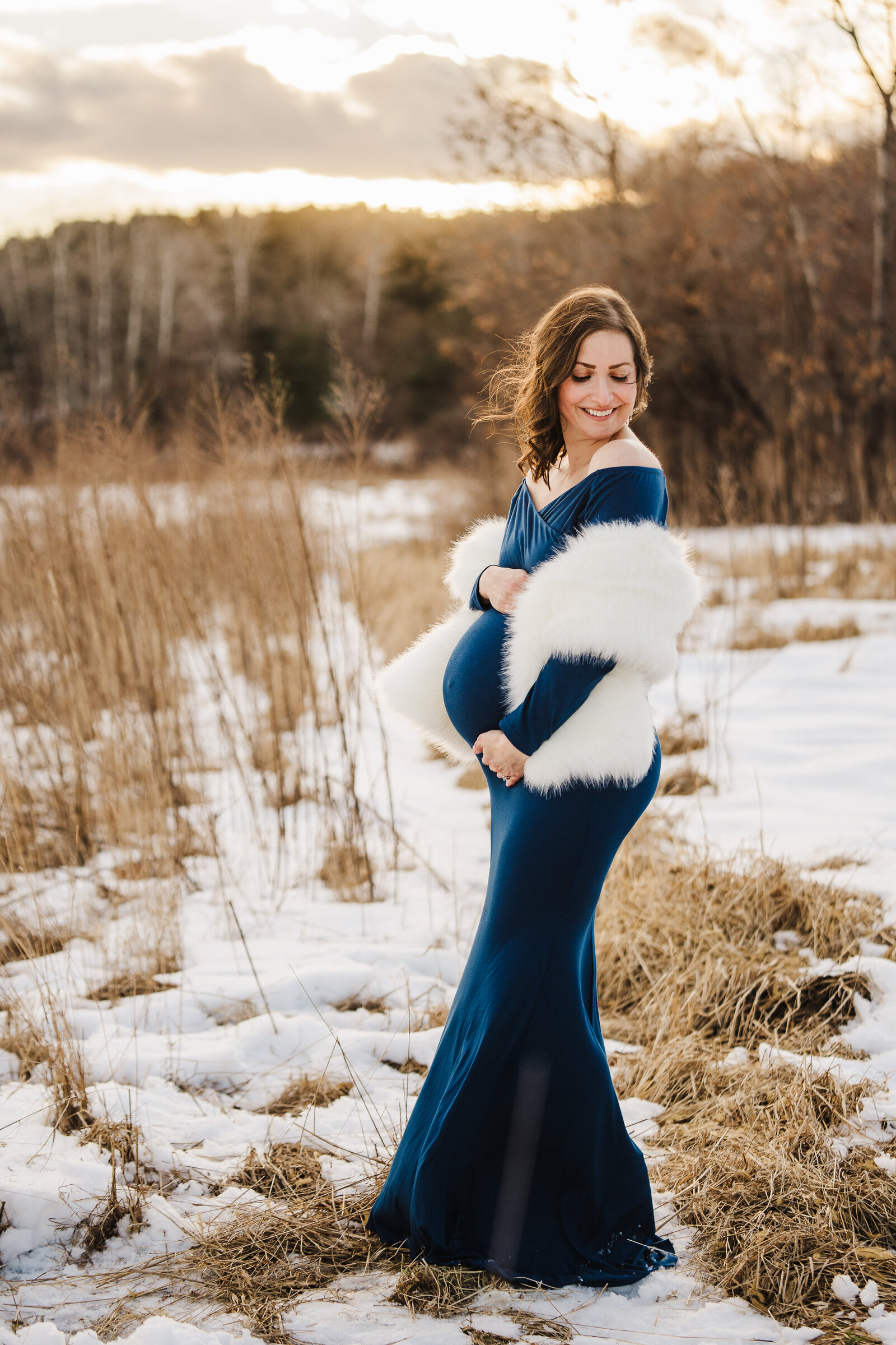 pregnant woman in blue dress stands in snowy field