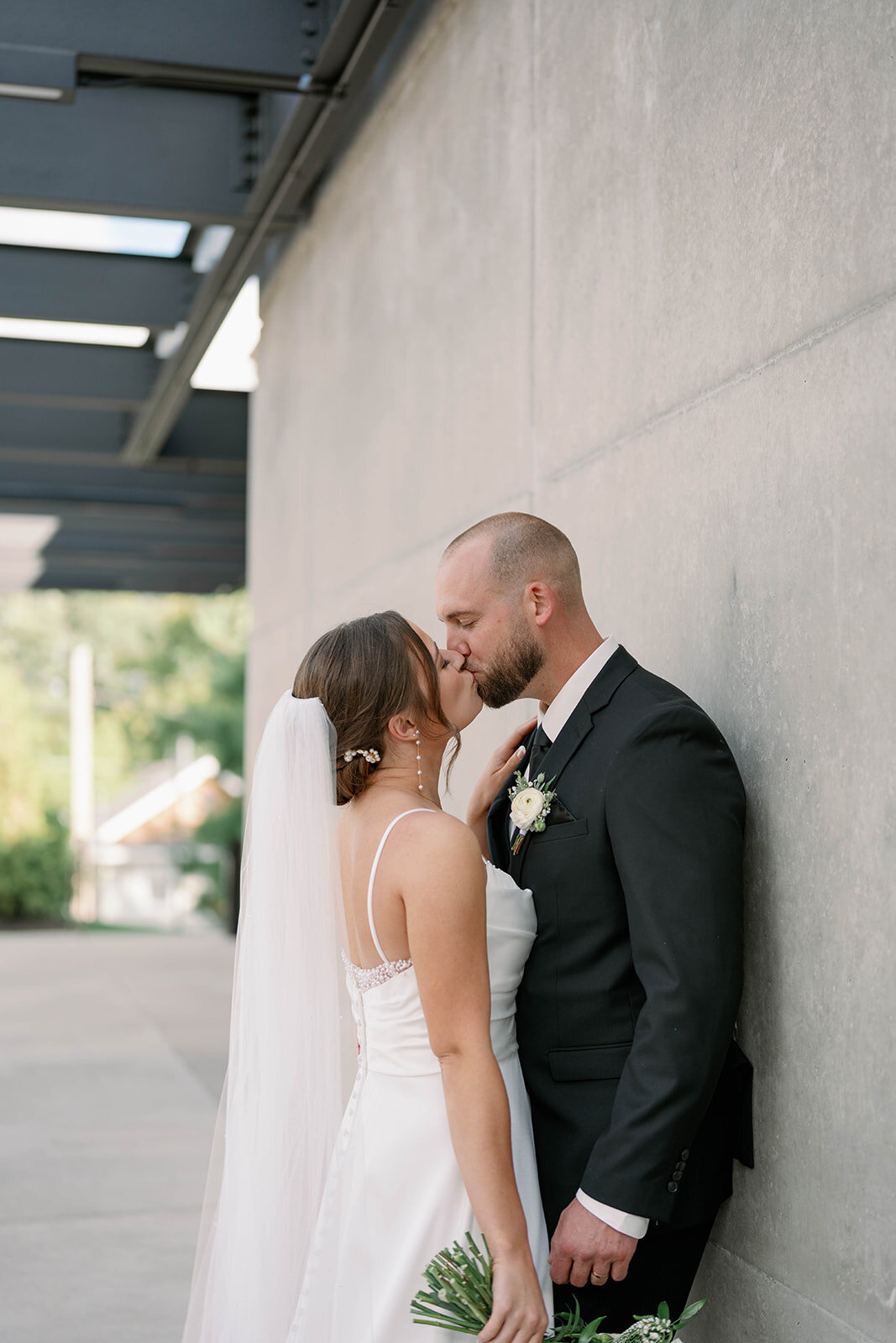 Bride and groom sharing a kiss by a modern concrete wall during an elegant Michigan wedding.