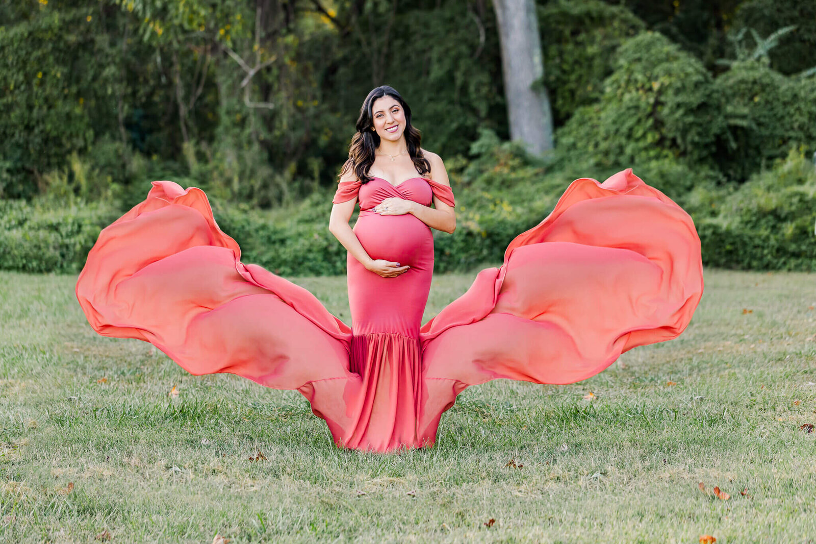 A beautiful pregnant woman posing at a Woodbridge park with her pink dress tossed in the wind.