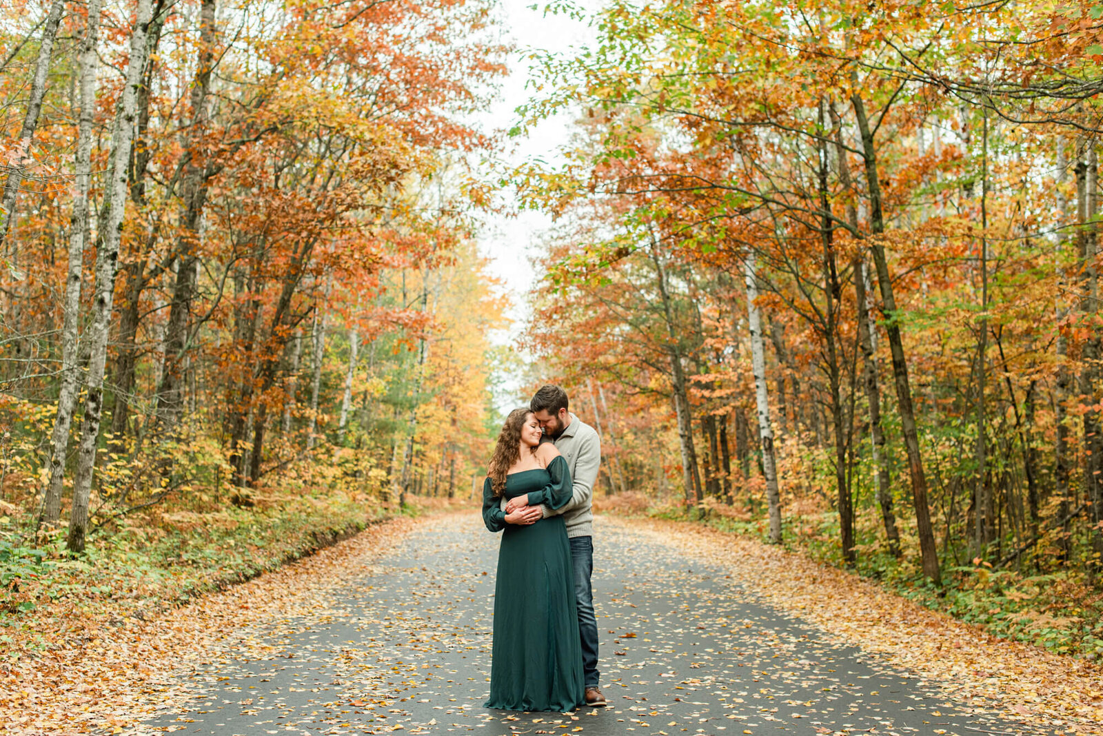 A couple holding each other on a road, surrounded by beautiful fall colors in a northern Wisconsin engagement photography session