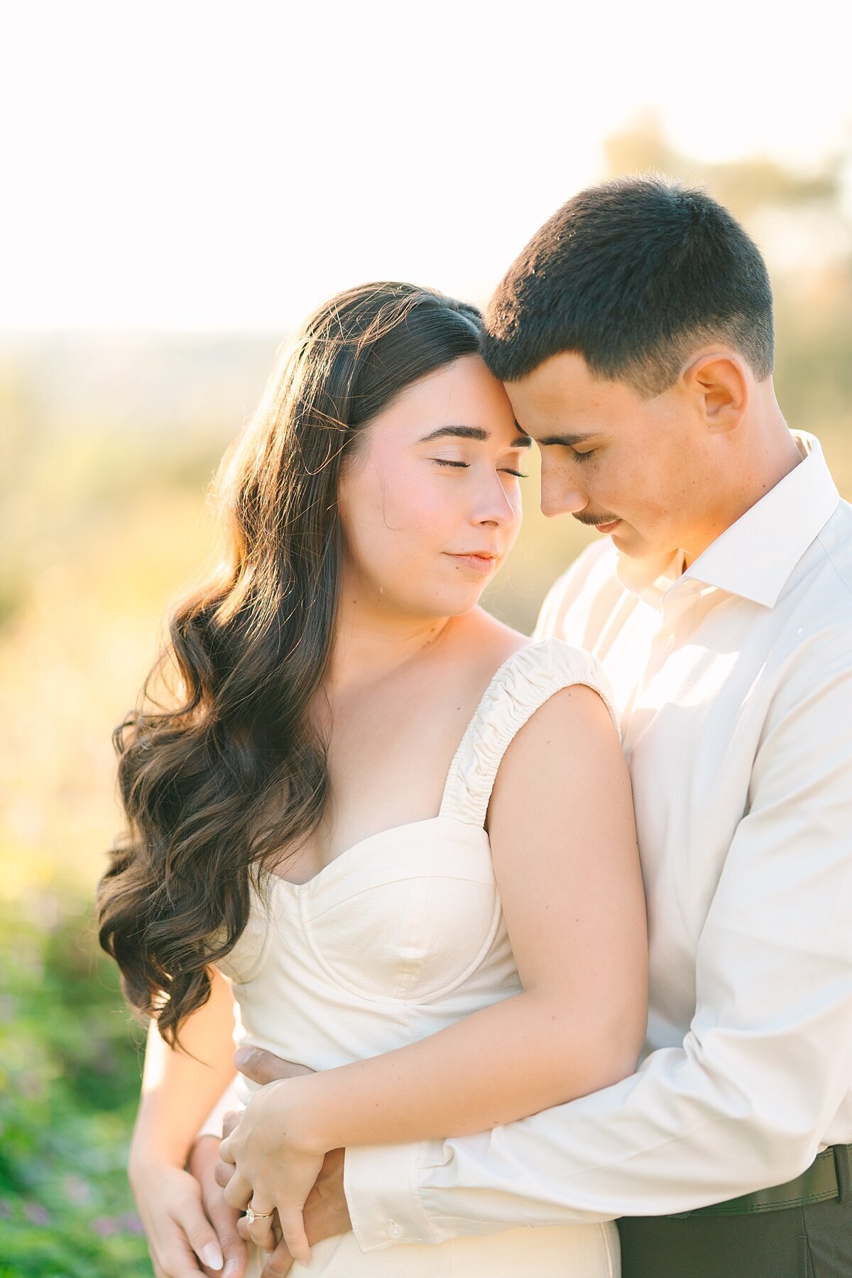 Engaged couple snuggling in to one another during their engagement photoshoot at Alta Vista Botanical Gardens in Vista, CA.