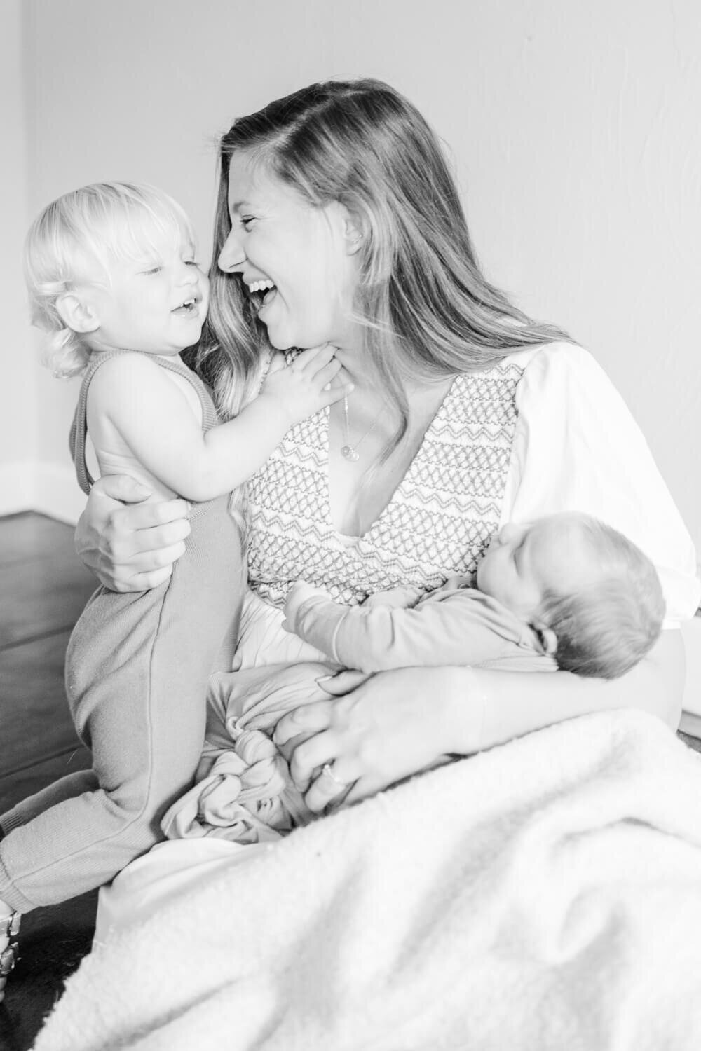 Mother holds newborn and laughs with her happy toddler, black and white