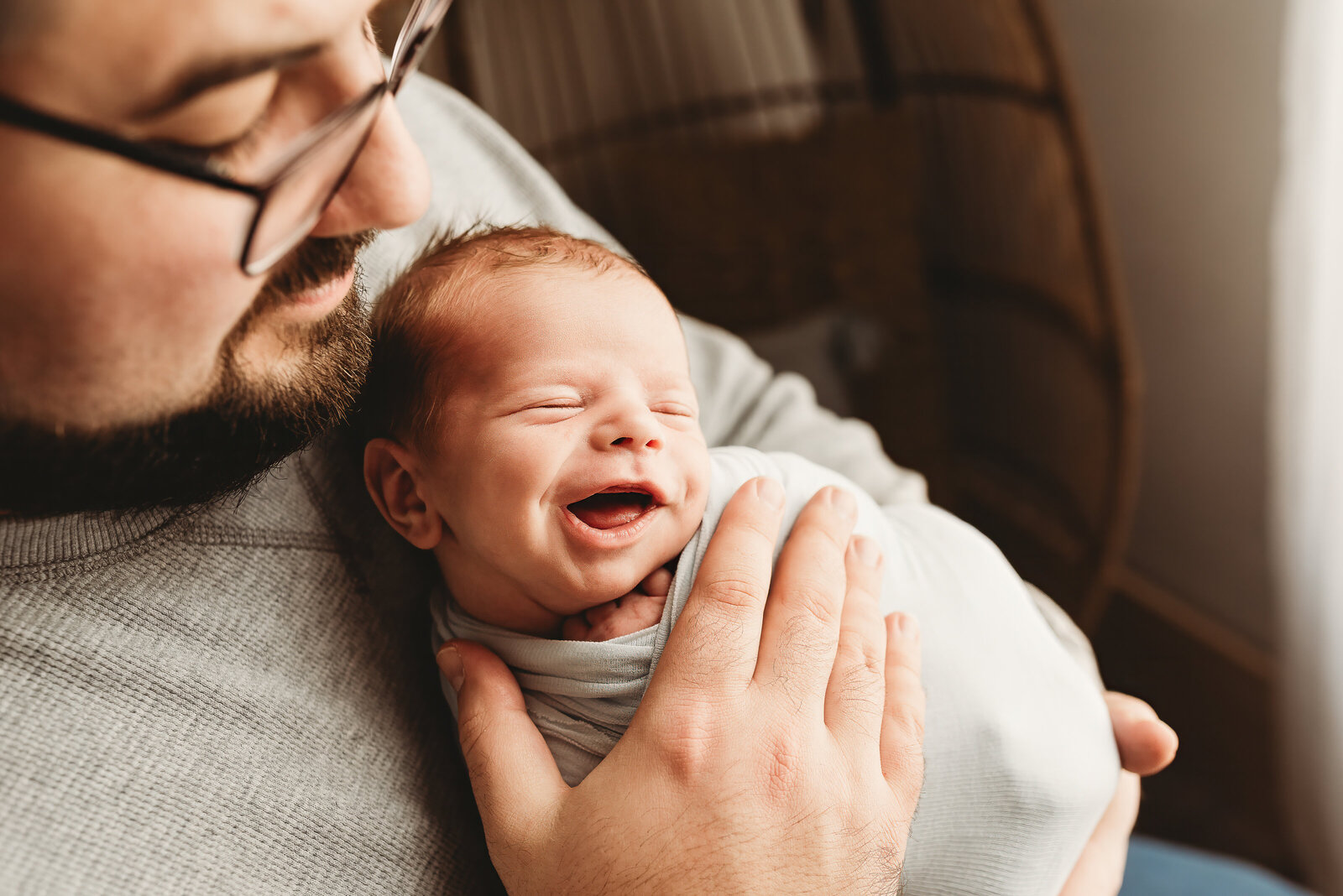 A newborn baby boy smirks at the camera while his dad holds him tight during some father-son pictures at a studio newborn session.