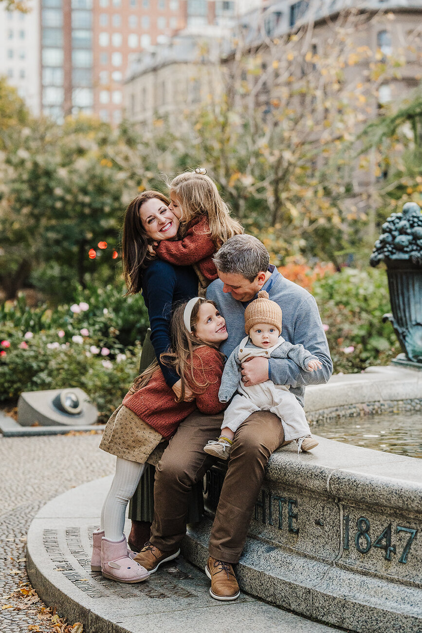 family sits on the side of a fountain in boston public garden