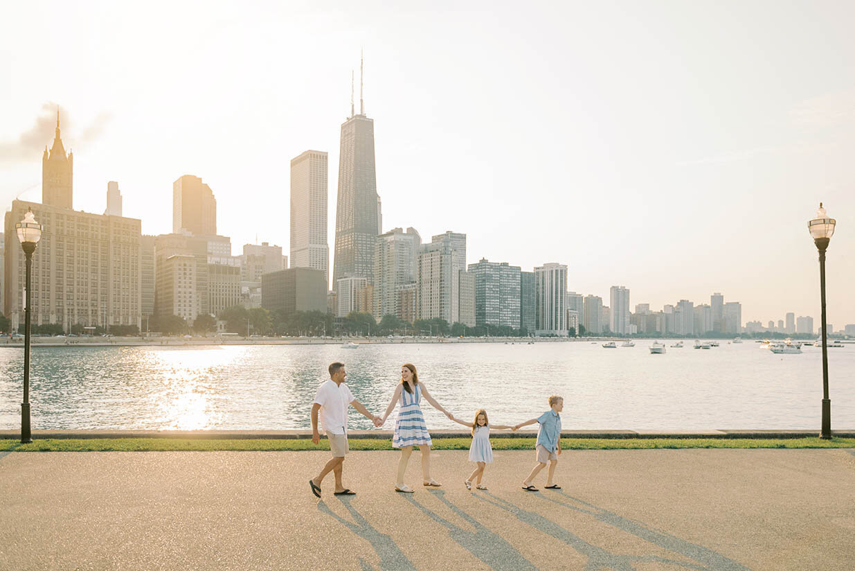 Family of four walking in Milton Olive Lee Park with the Chicago skyline behind them for their Chicago family photos
