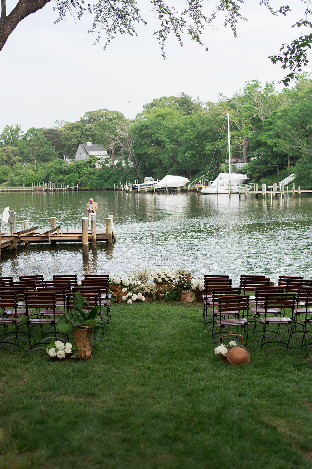 Waterfront micro-wedding ceremony set up overlooking a pier, with neutral brown chairs and brown wicker baskets filled with white flowers.