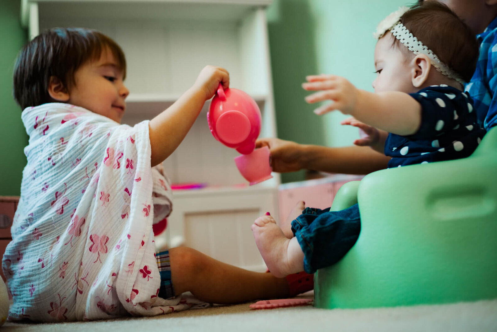 A brother and sister share a pretend pot of tea.