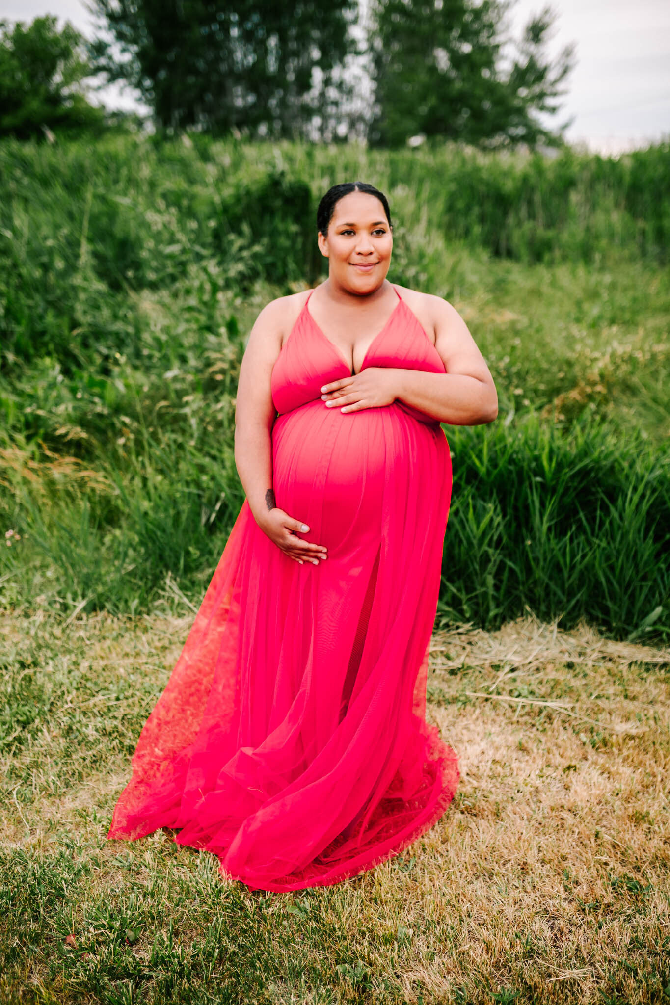 woman in a pink dress stands holding her pregnant belly during her maternity session.