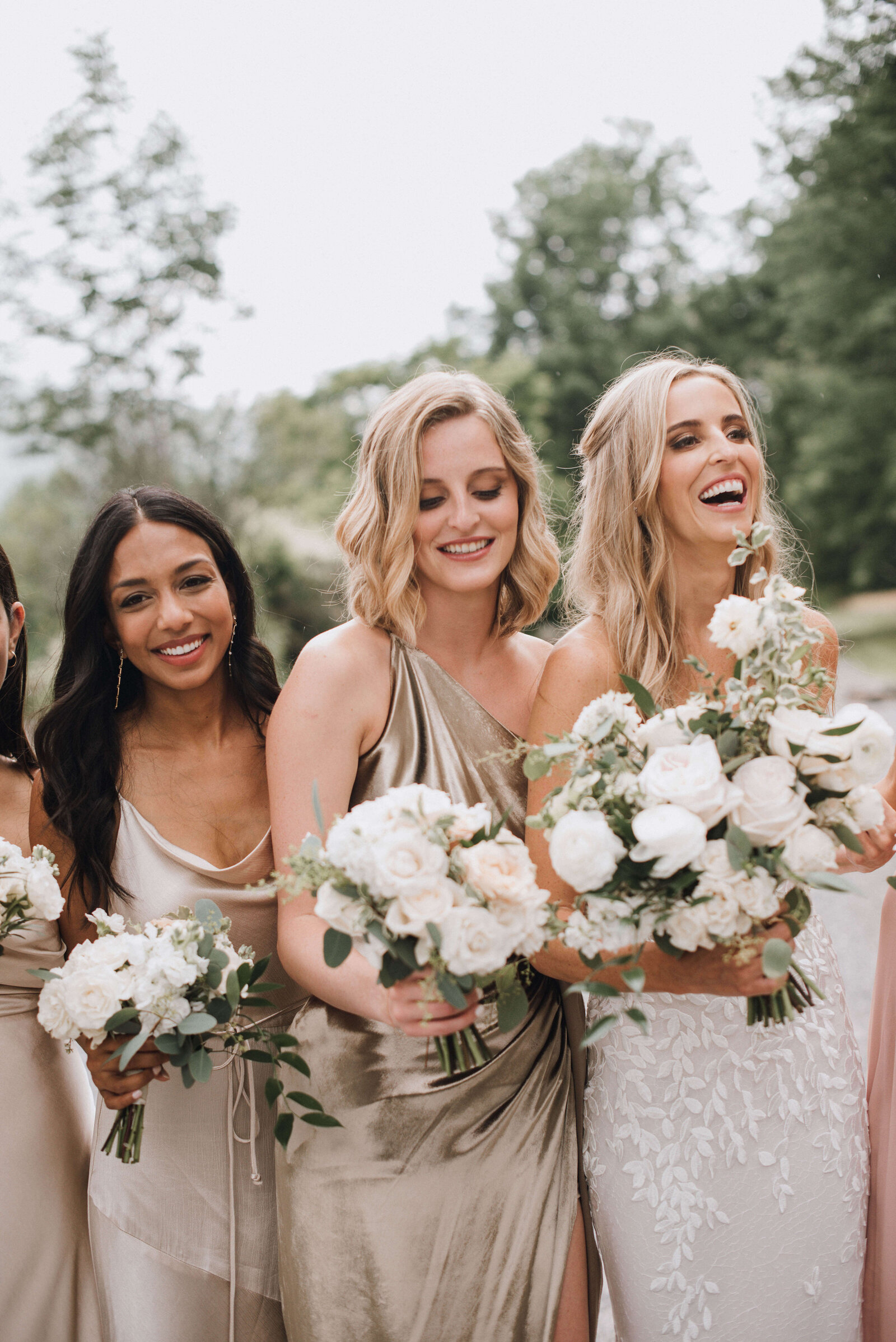 A bride and her bridessmaids in shapes of ivory and champagne are holding white bouquets