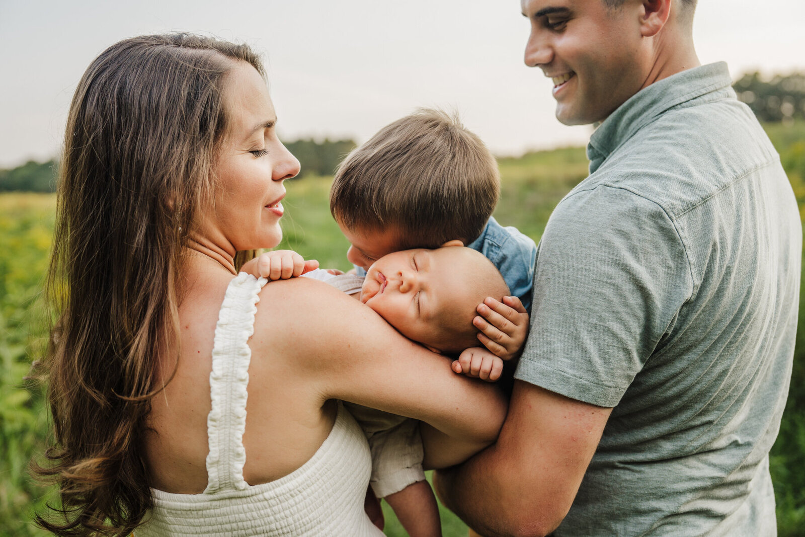 toddler boy hugs baby brother in parents arms in an outdoor newborn session