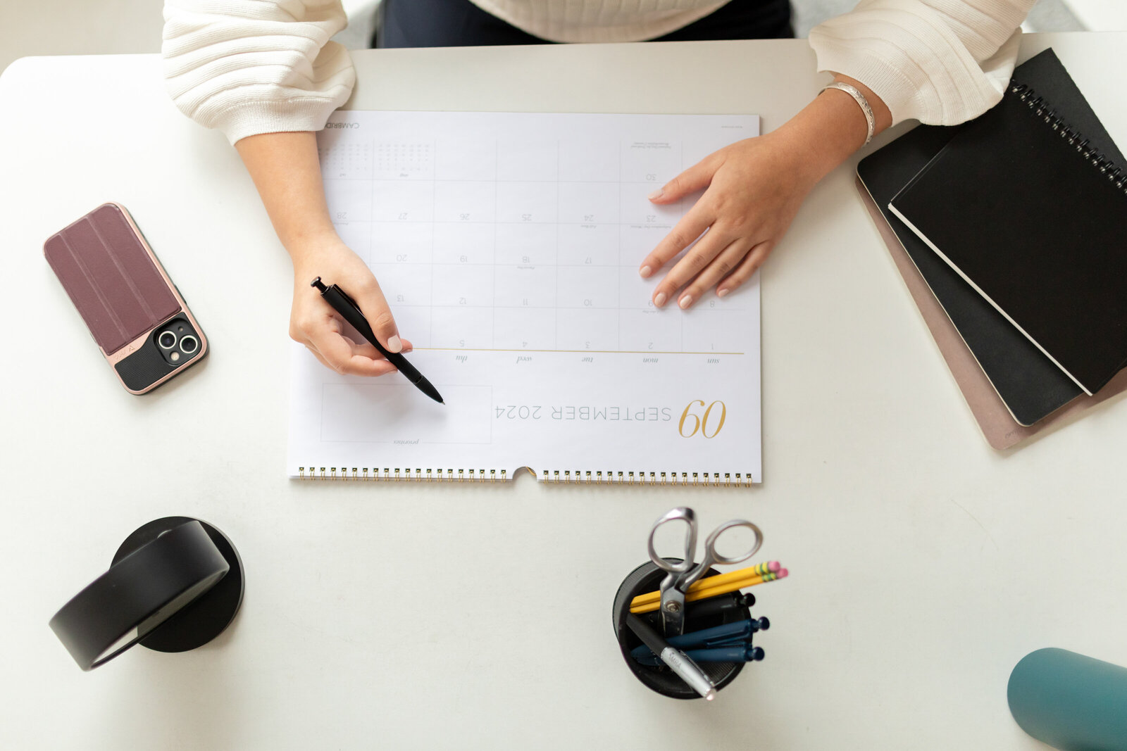 close up detail of woman writing on desk calendar for branding session, shot from top down