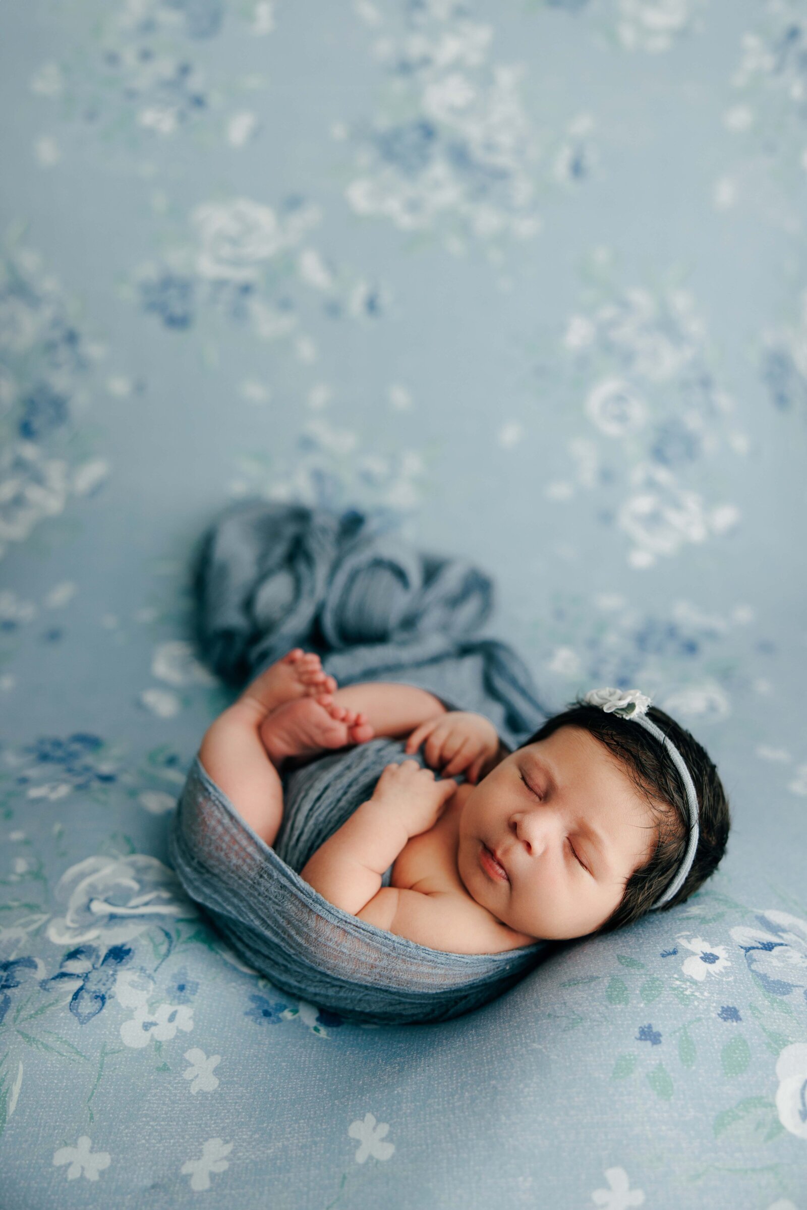 A chubby baby with dark hair lies on a blue floral backdrop