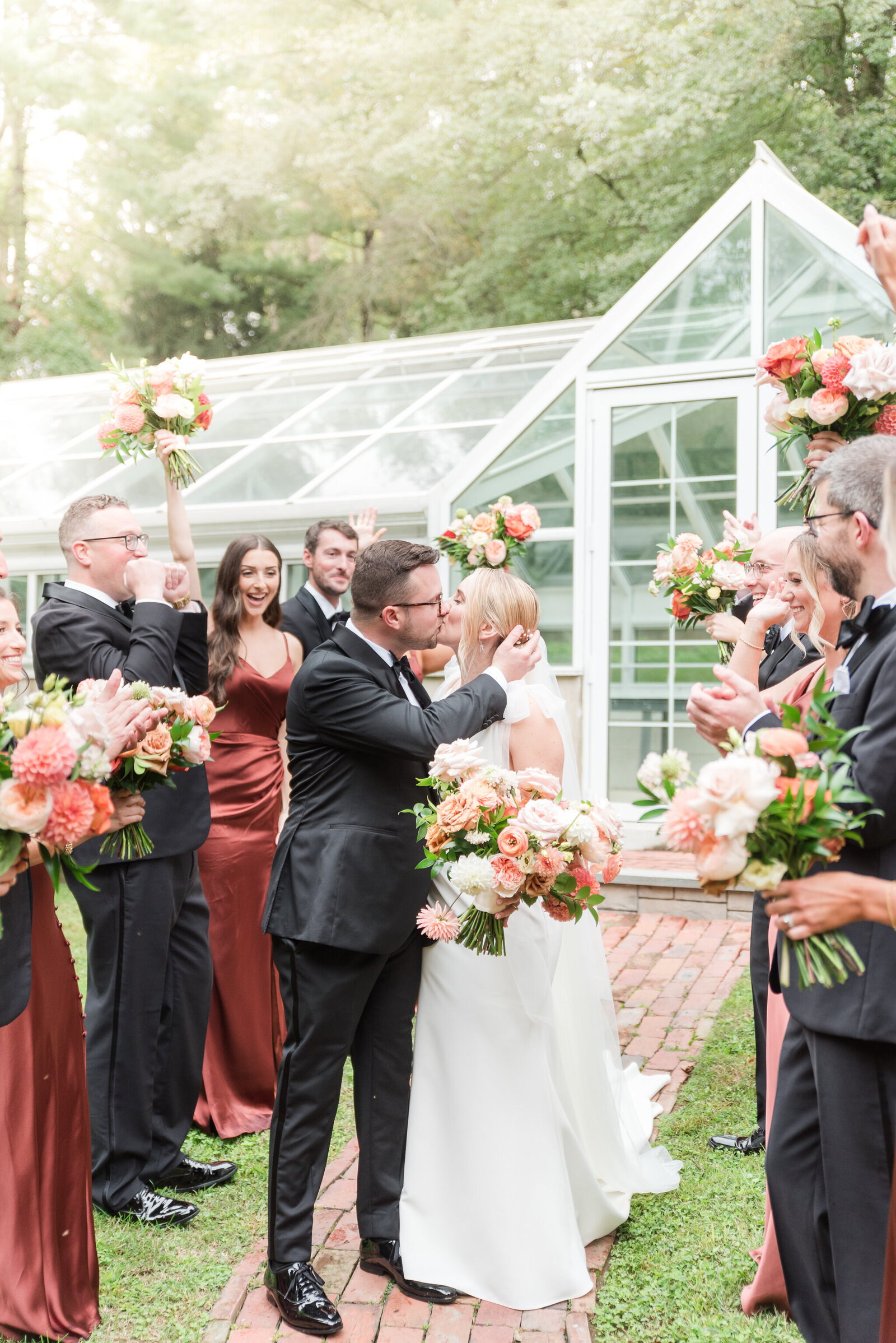 rust bridesmaids dresses and black tuxedos wedding party excitedly waving happy couple