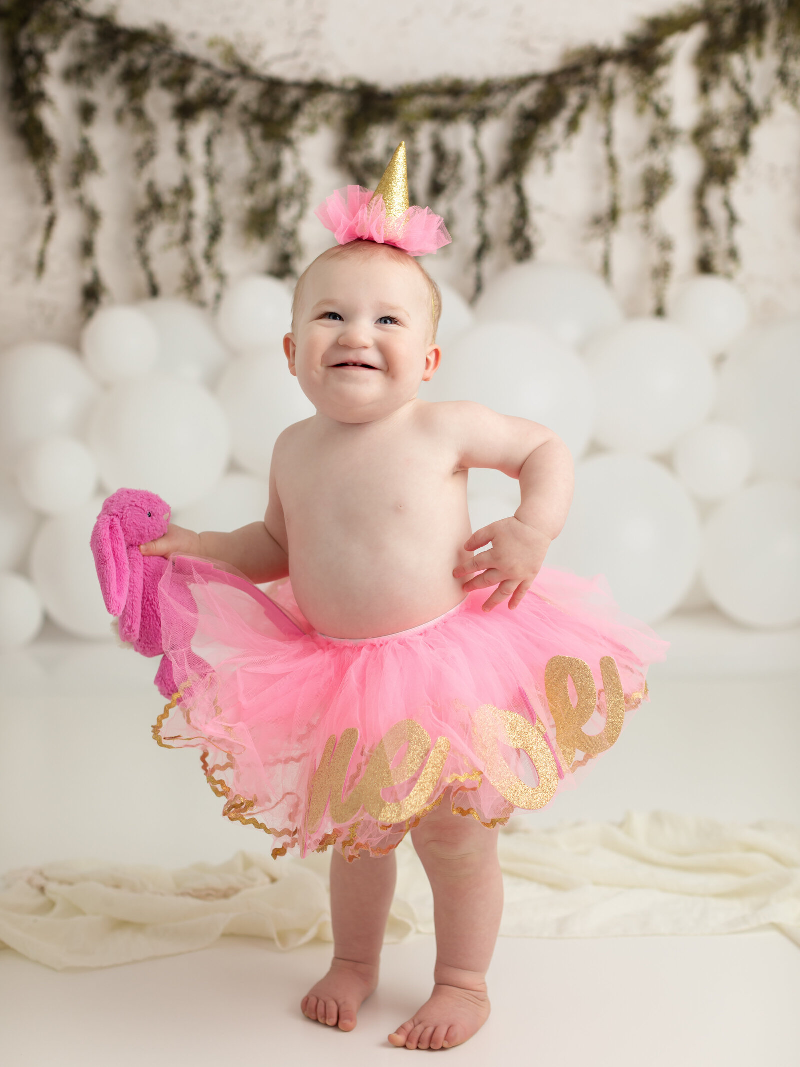 one year old girl in pink tutu smiling for first birthday photoshoot