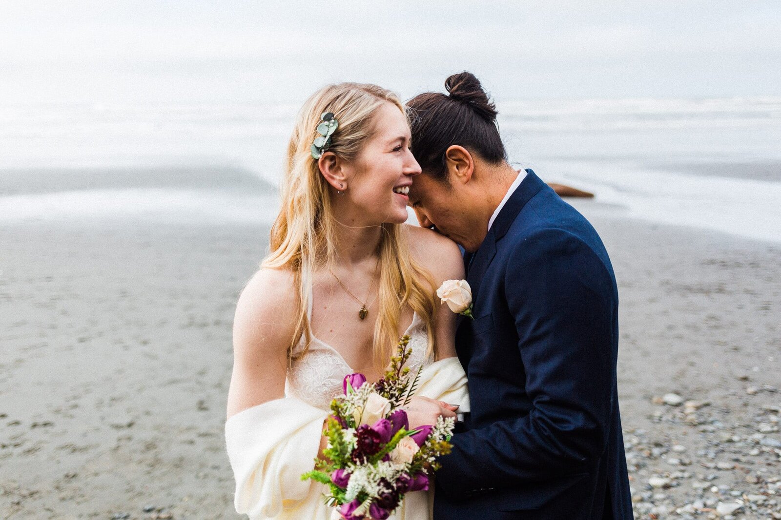 groom kissing bride on shoulder at beach