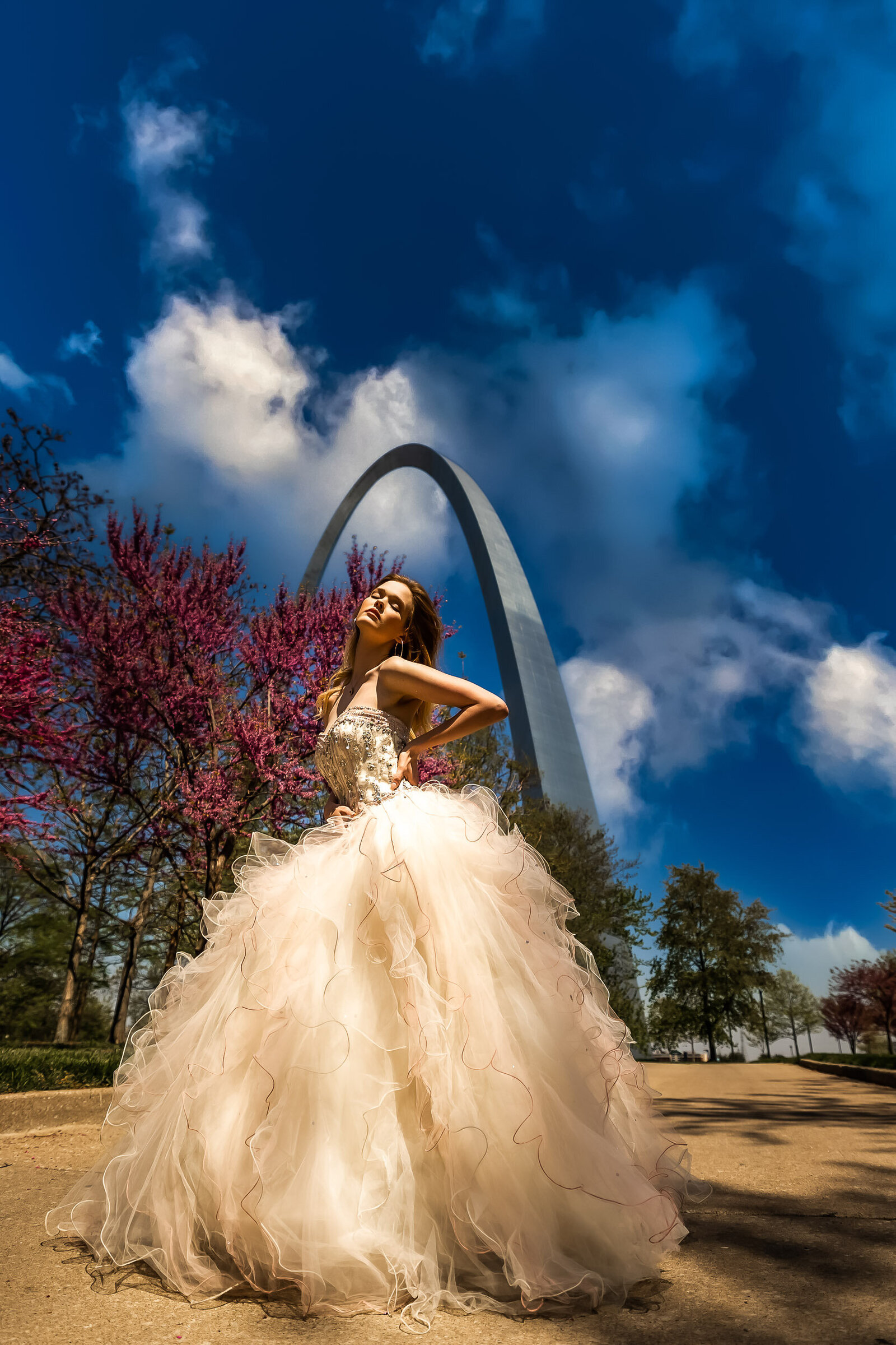 senior in pink, princess ball gown with her eyes closed in a full body frame underneath the Gateway Arch