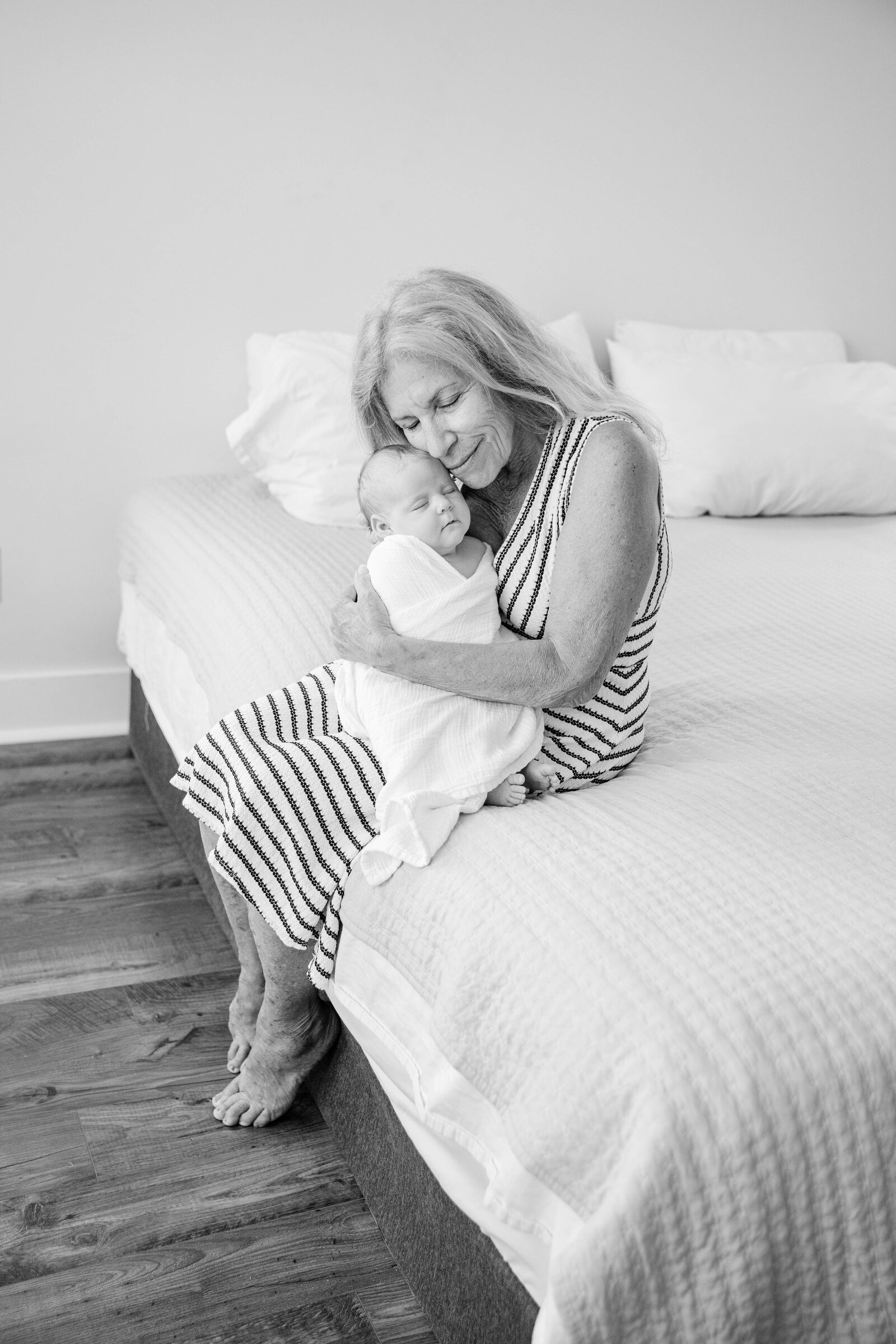 A black and white photo of a grandmother holding a baby on a bed, taken by a talented Bluffton Newborn Photographer.