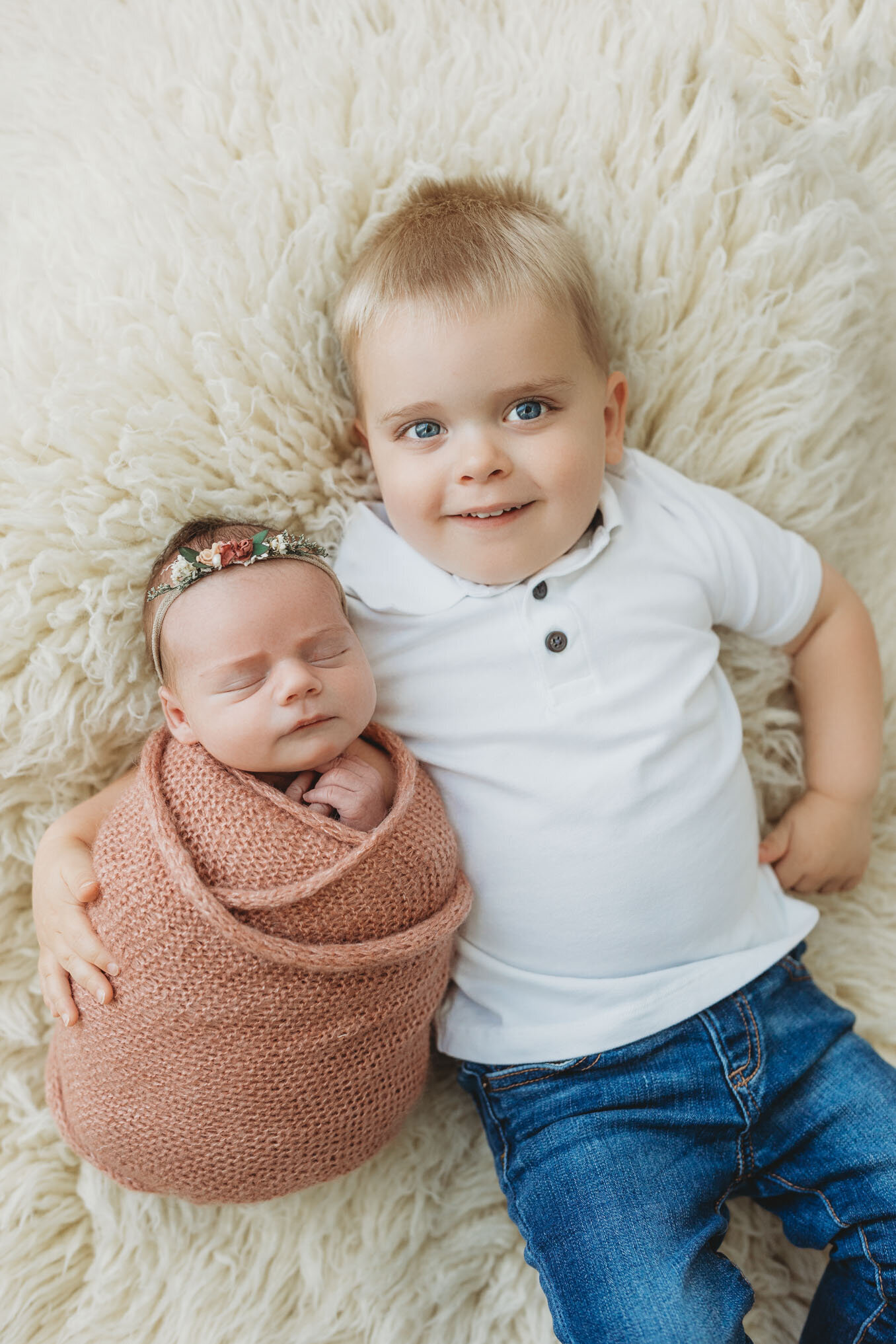 Toddler boy with his arm around his newborn baby sister
