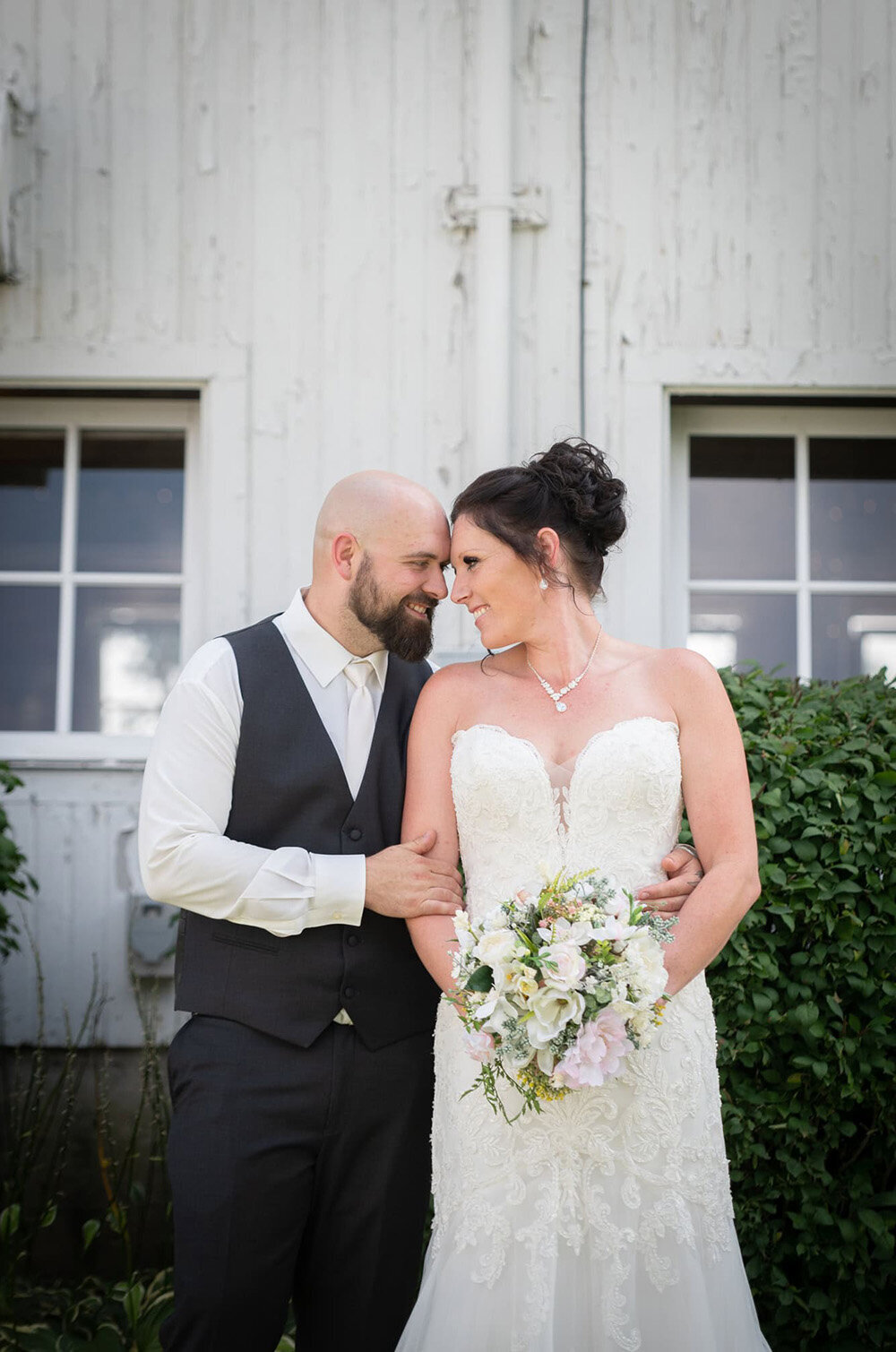 bride and groom put foreheads together in front of white barn