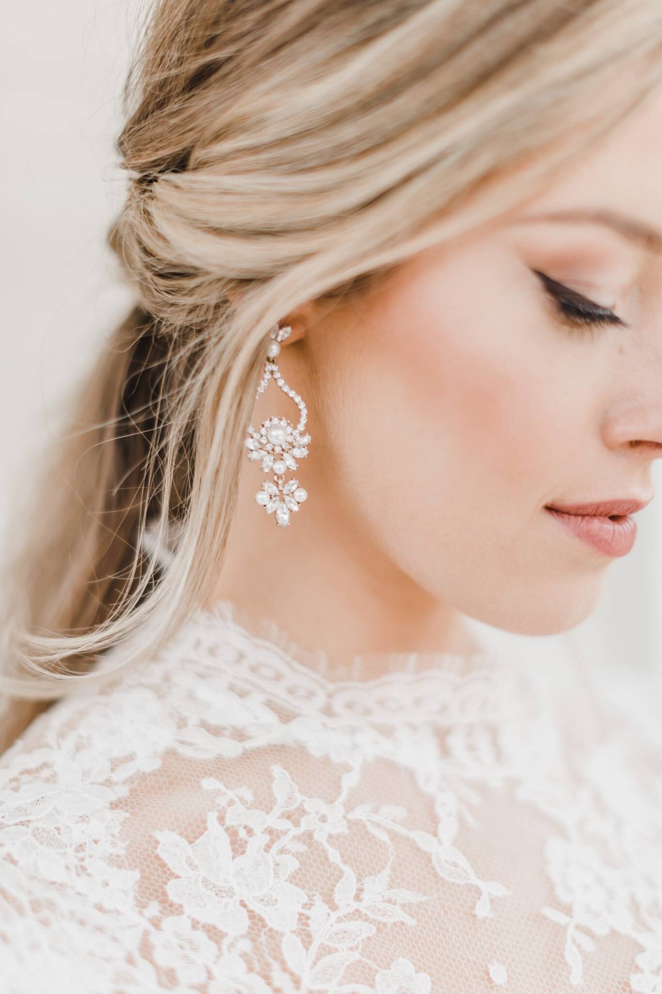 Closeup shot of bride with blond hair showing one side of her face, focusing in on her earrings and makeup