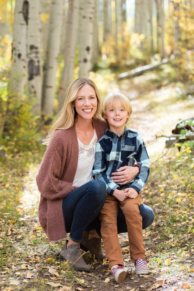 a mom in a maroon sweater gives her son a hug in an aspen grove