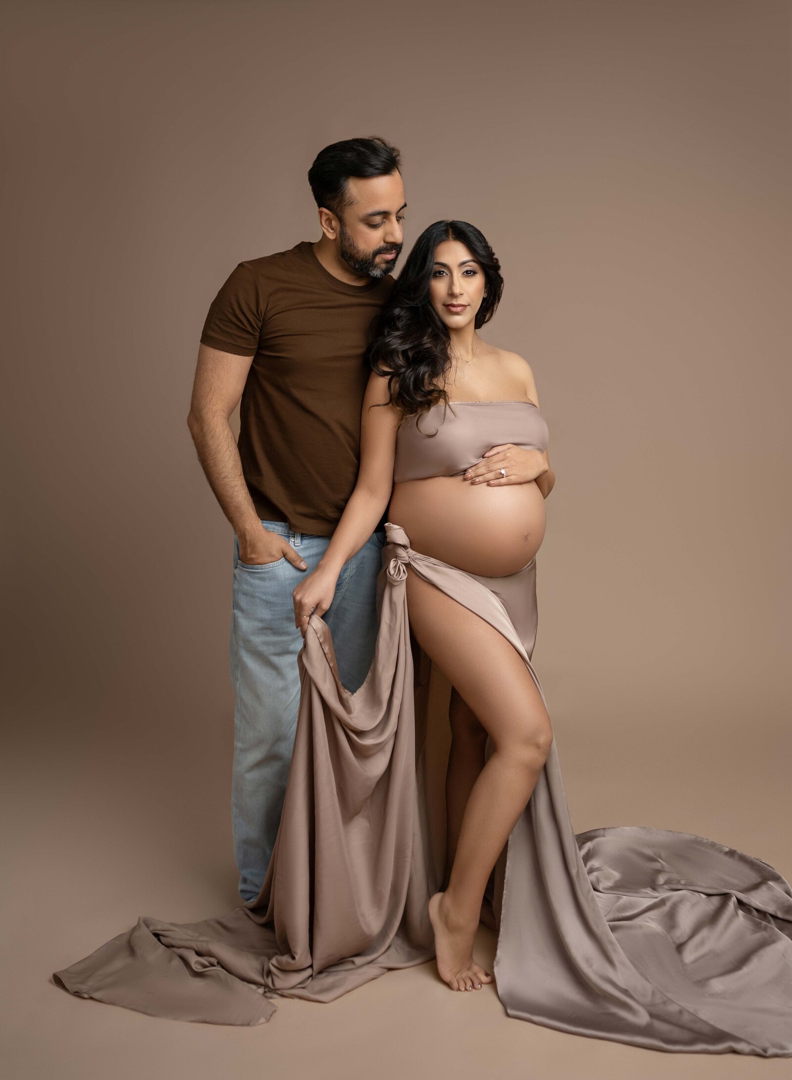 Maternity couple pose of Dad look at Mom as she is holding draped fabric shirt under her baby bump. Photo taken at Atlanta Maternity photo studio in Woodstock, GA.