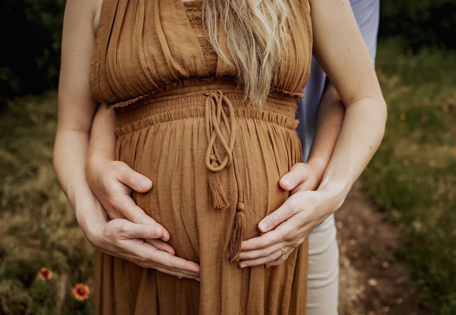 expectant mom and dad hold hands on her pregnant belly