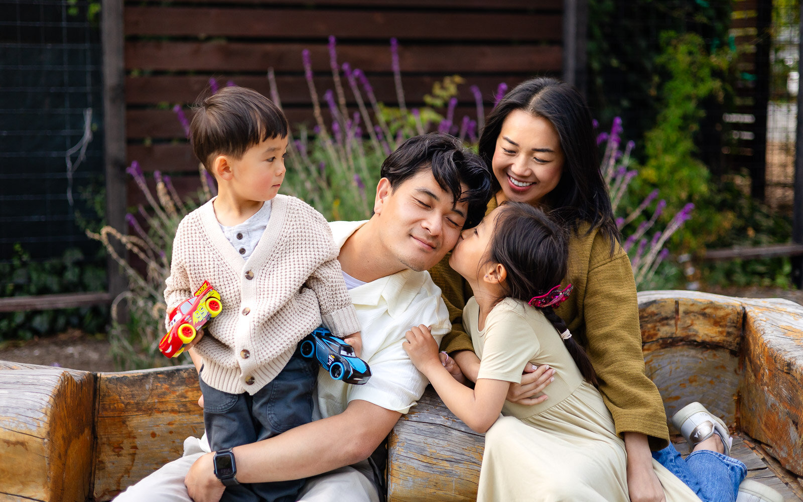 Family sitting together with kids and toy cars in garden setting – Family Photographer Ellobelle Photography