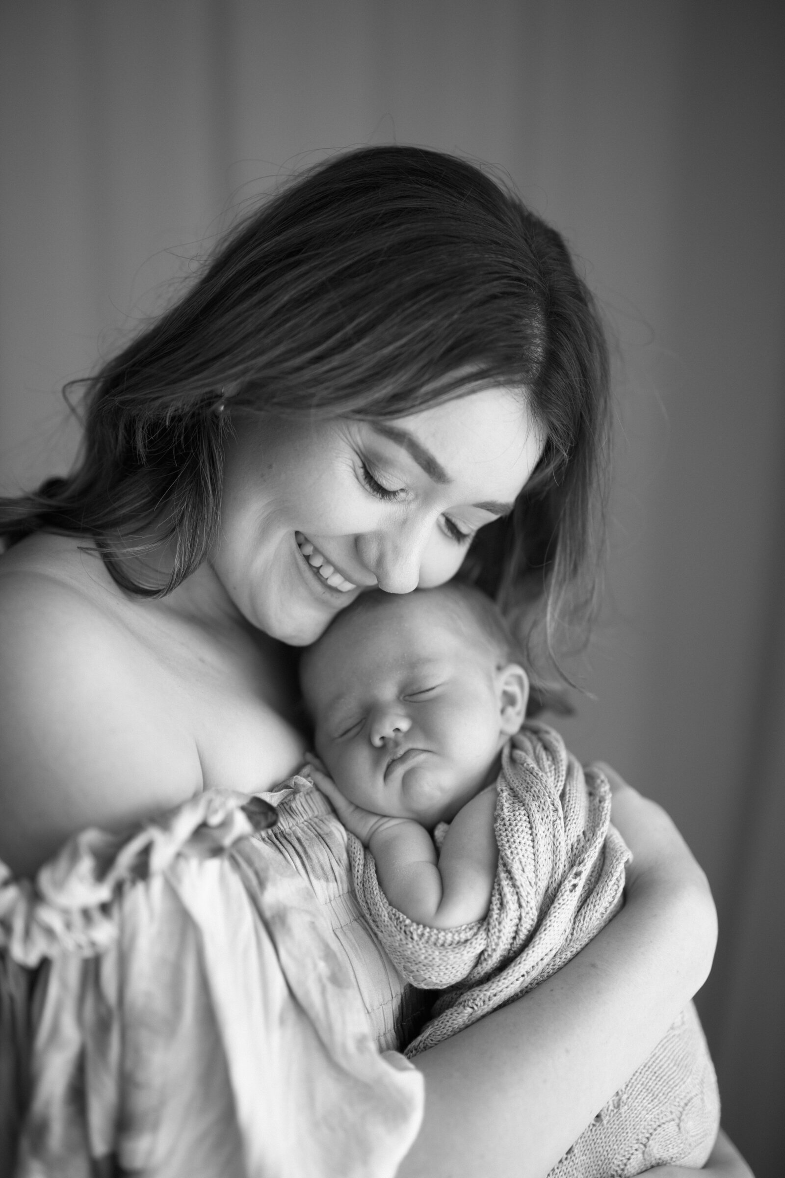 Best newborn family photographer in Perth capturing a tender moment between parents and their newborn in a cozy studio setting.