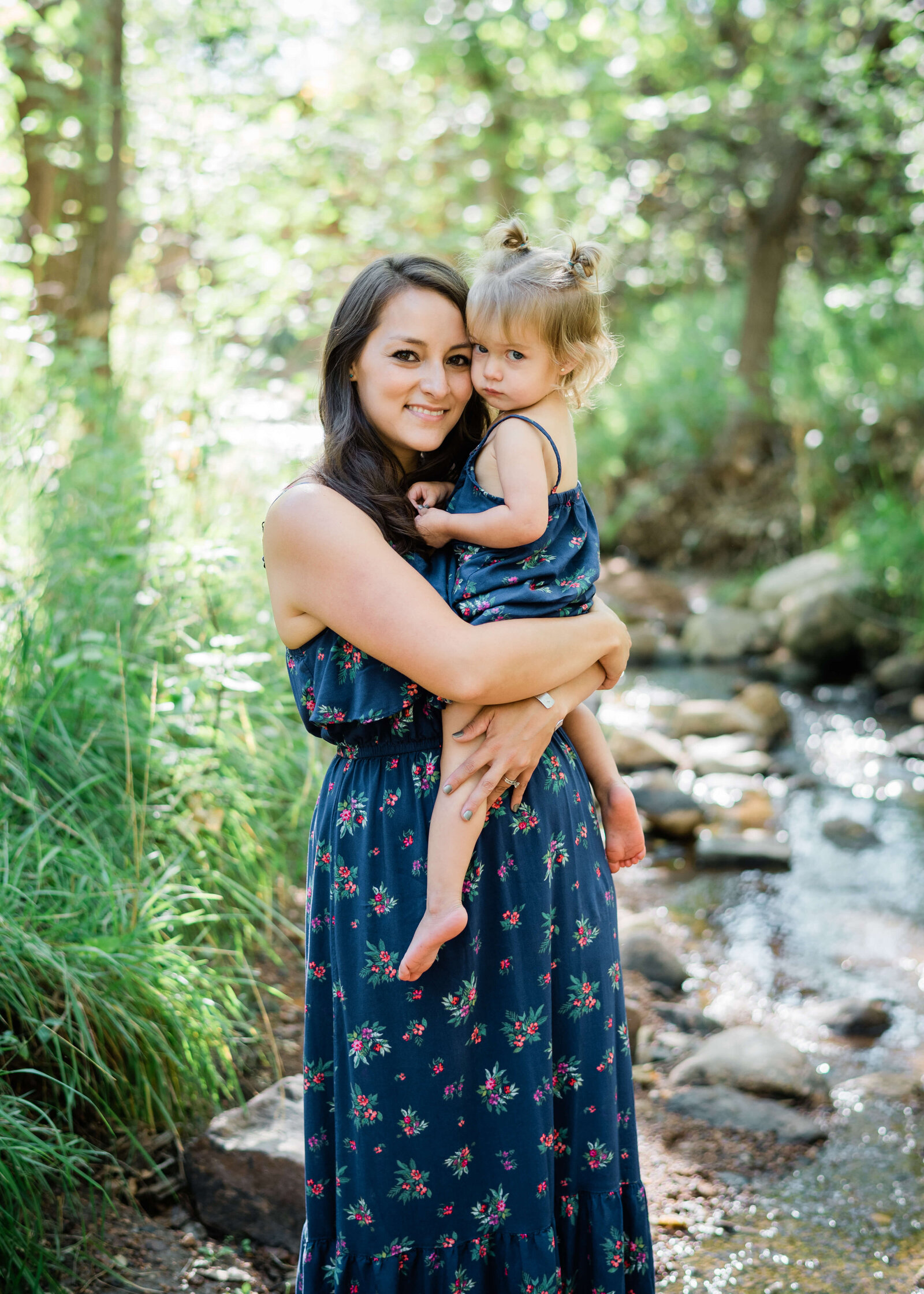 Northern Virginia family photographer captures an image of a brunette mother holding her toddler daughter, they are wearing matching navy dresses and are standing in a stream