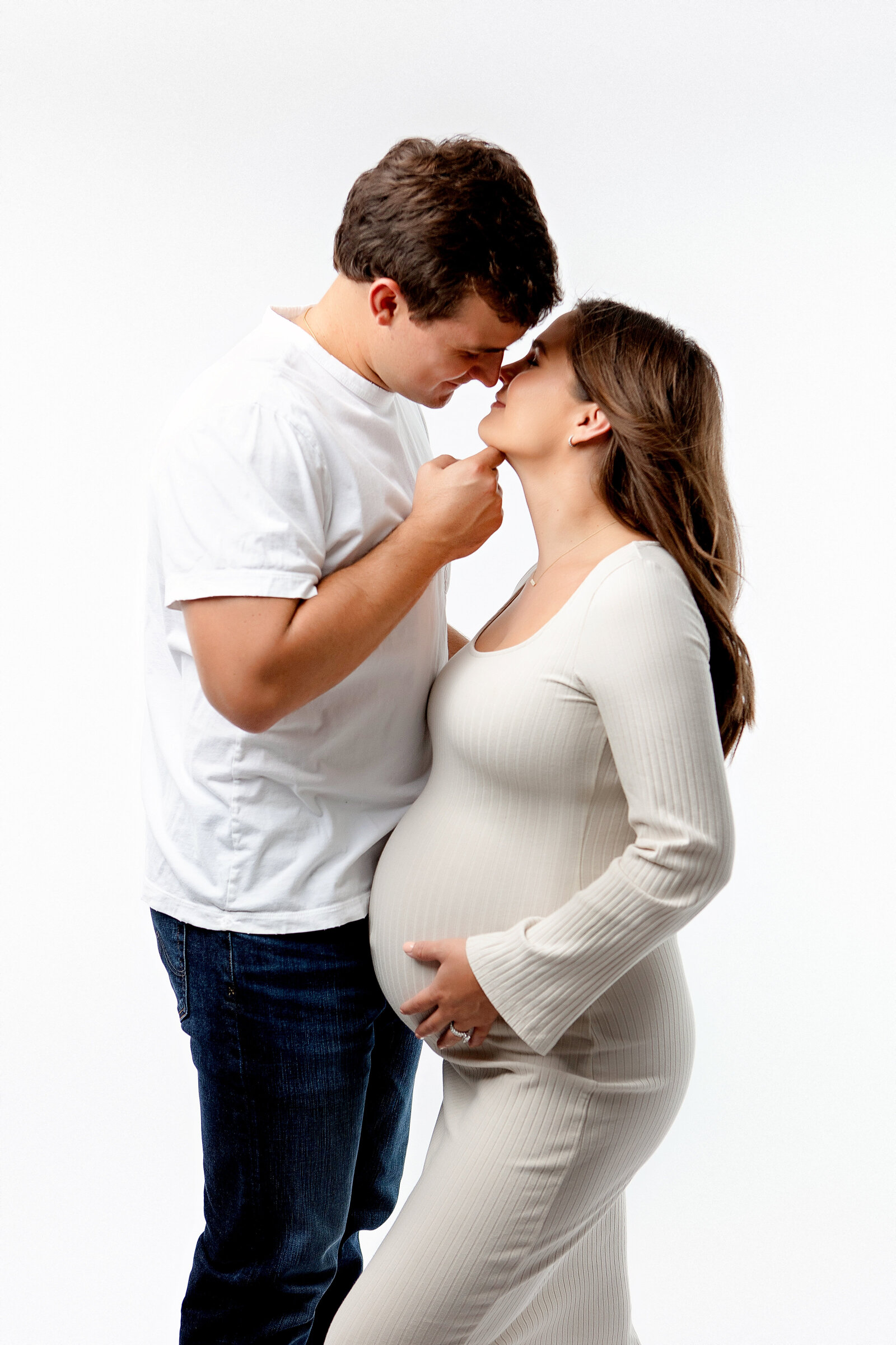 husband and wife maternity photos. expectant mother wearing  fitted white dress while husband lifts chin for an intimate kiss. Fr4esno, Clovis, Maternity Photographer