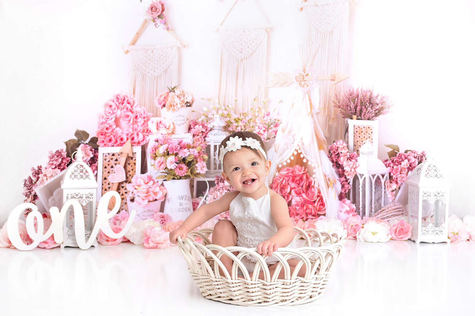 girl sits in whicker basket at her first birthday shoot