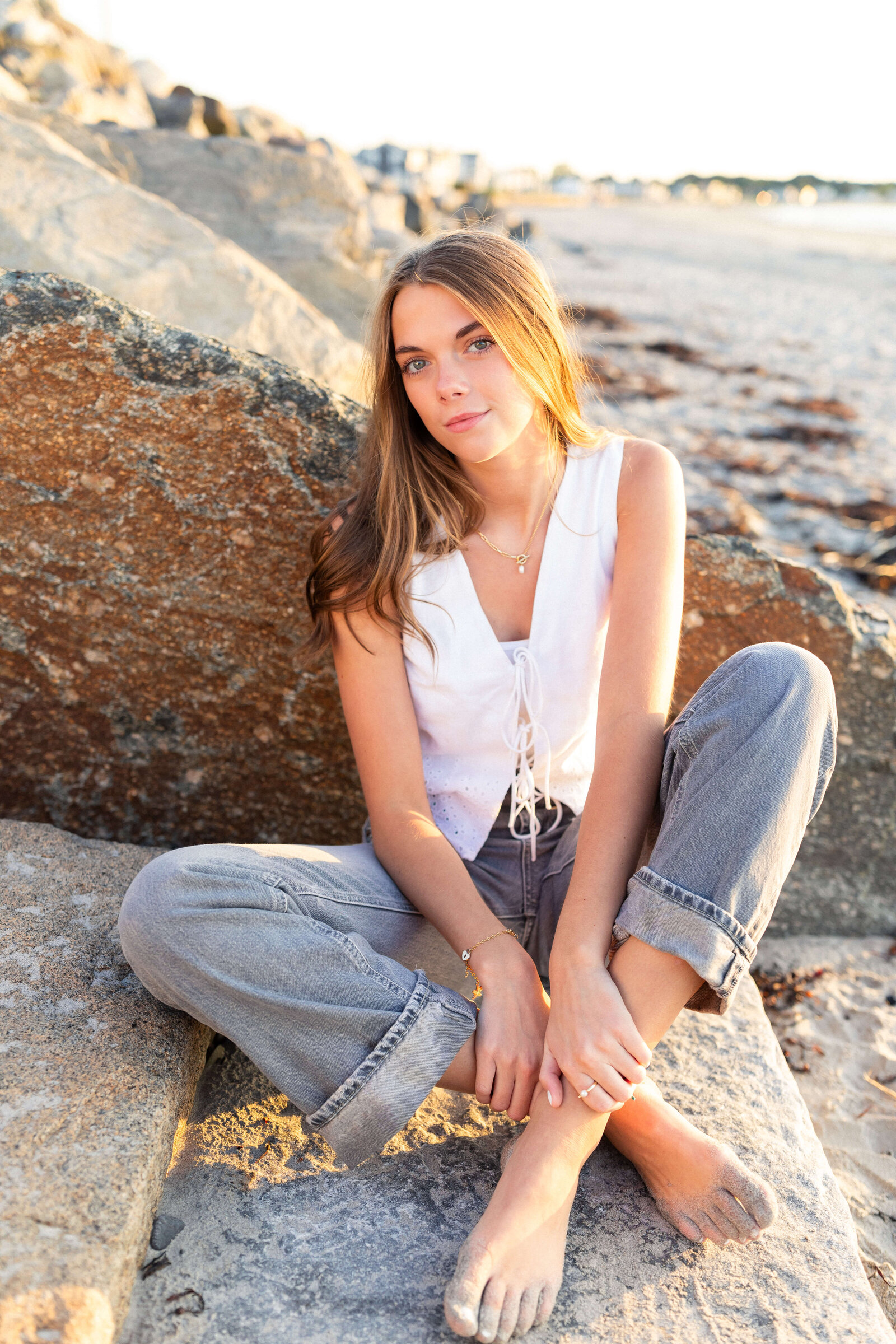 brunette high schooler posing on a beach wearing a white shirt