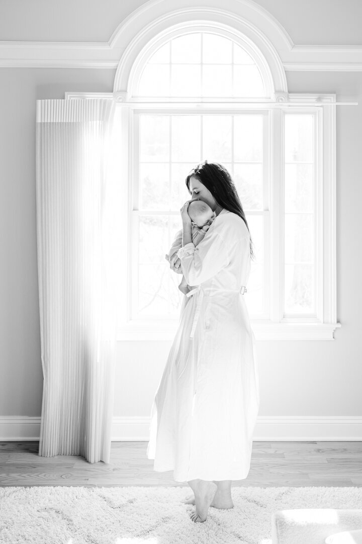 high key black and white image of mother holding baby girl in front of a beautiful window